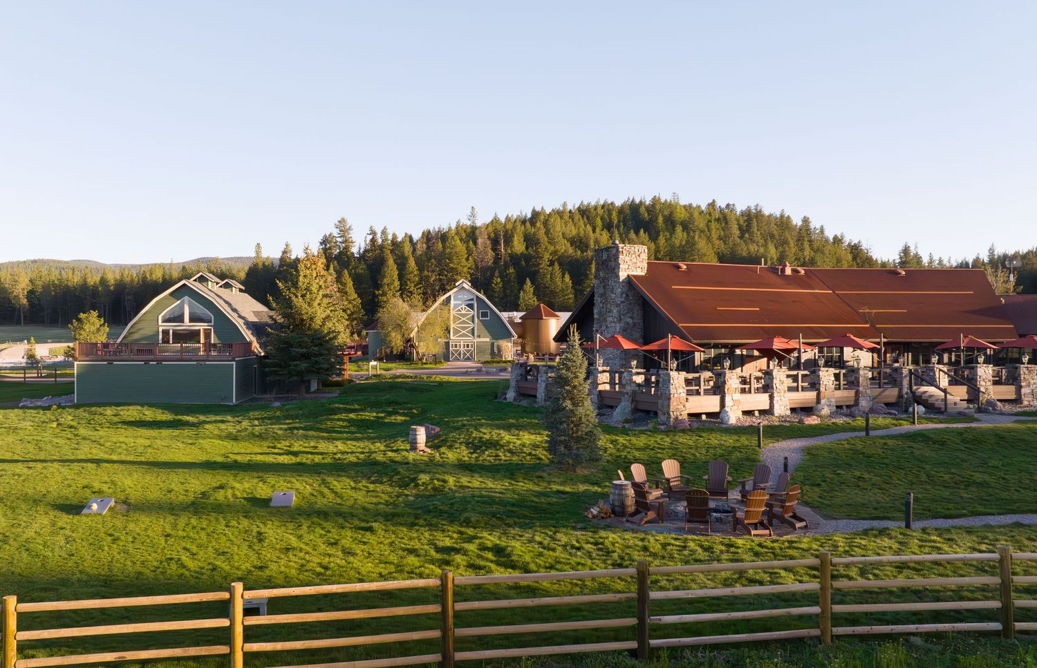 Rustic ranch lodge surrounded by green meadows and pine trees at golden hour.