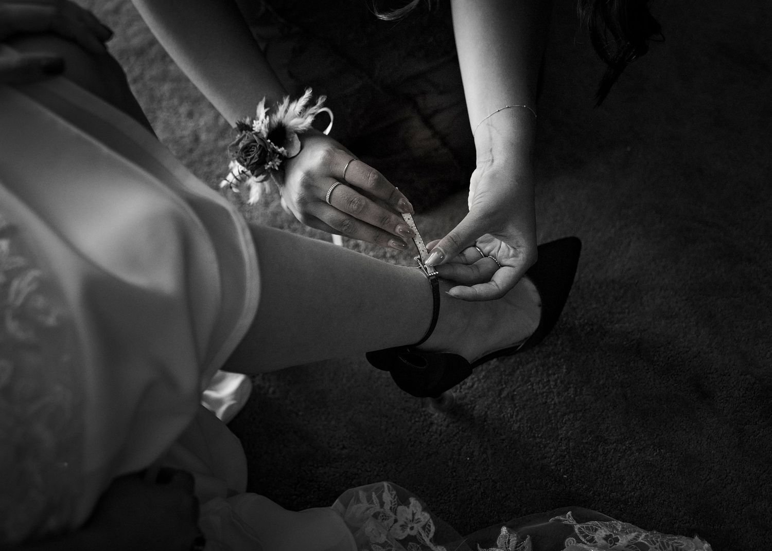 Black and white photo of hands fastening a bridal shoe on the bride's foot before the wedding ceremony.