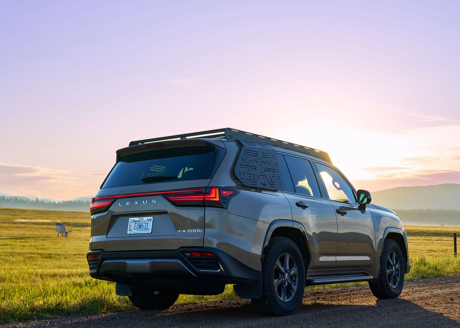 Rear view of gold Lexus LX SUV on dirt road during vibrant pink and purple sunset.
