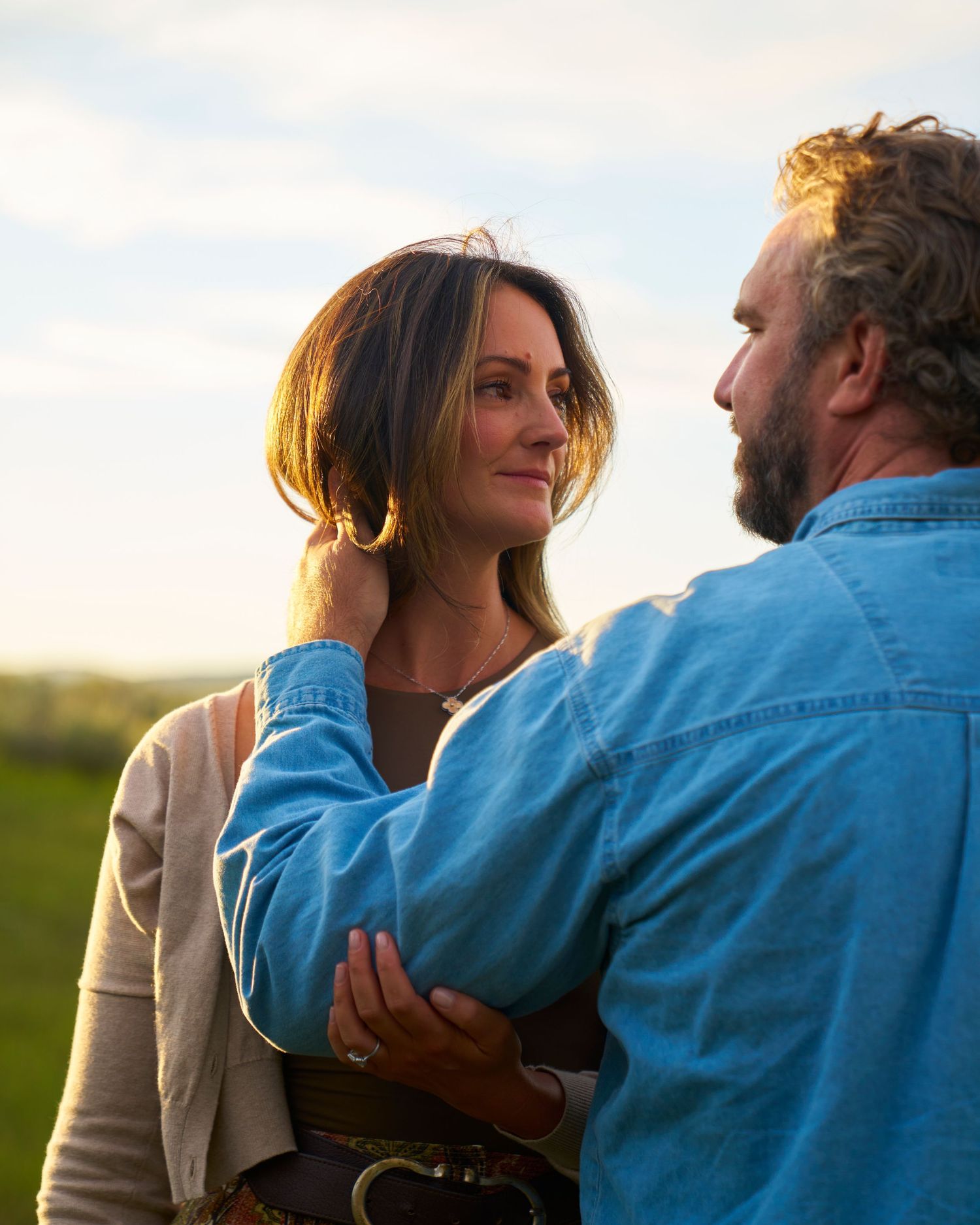 Man tenderly holds womans face as golden sunset light illuminates romantic outdoor couple portrait.