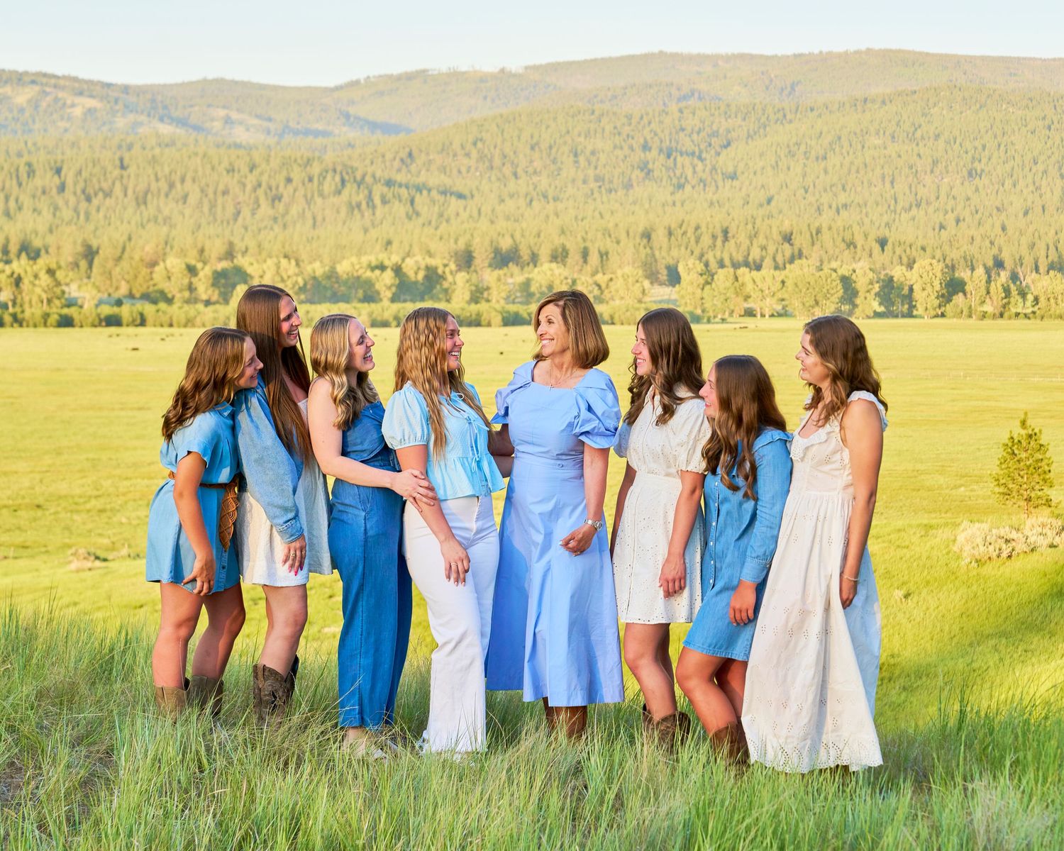 Group of eight women in blue and white dresses posing together in a scenic mountain meadow.