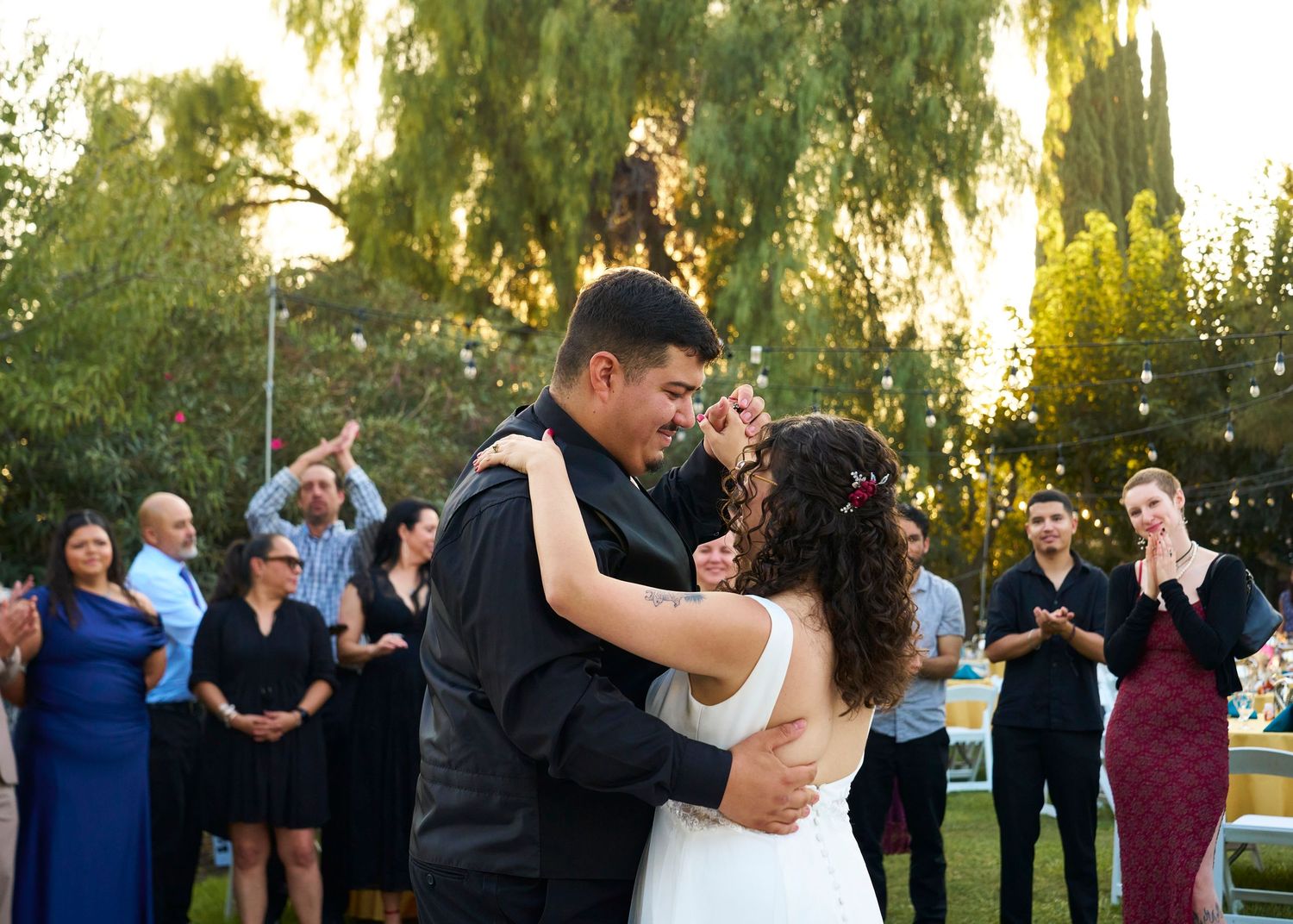 Couple shares first dance outdoors surrounded by applauding wedding guests at golden hour reception.