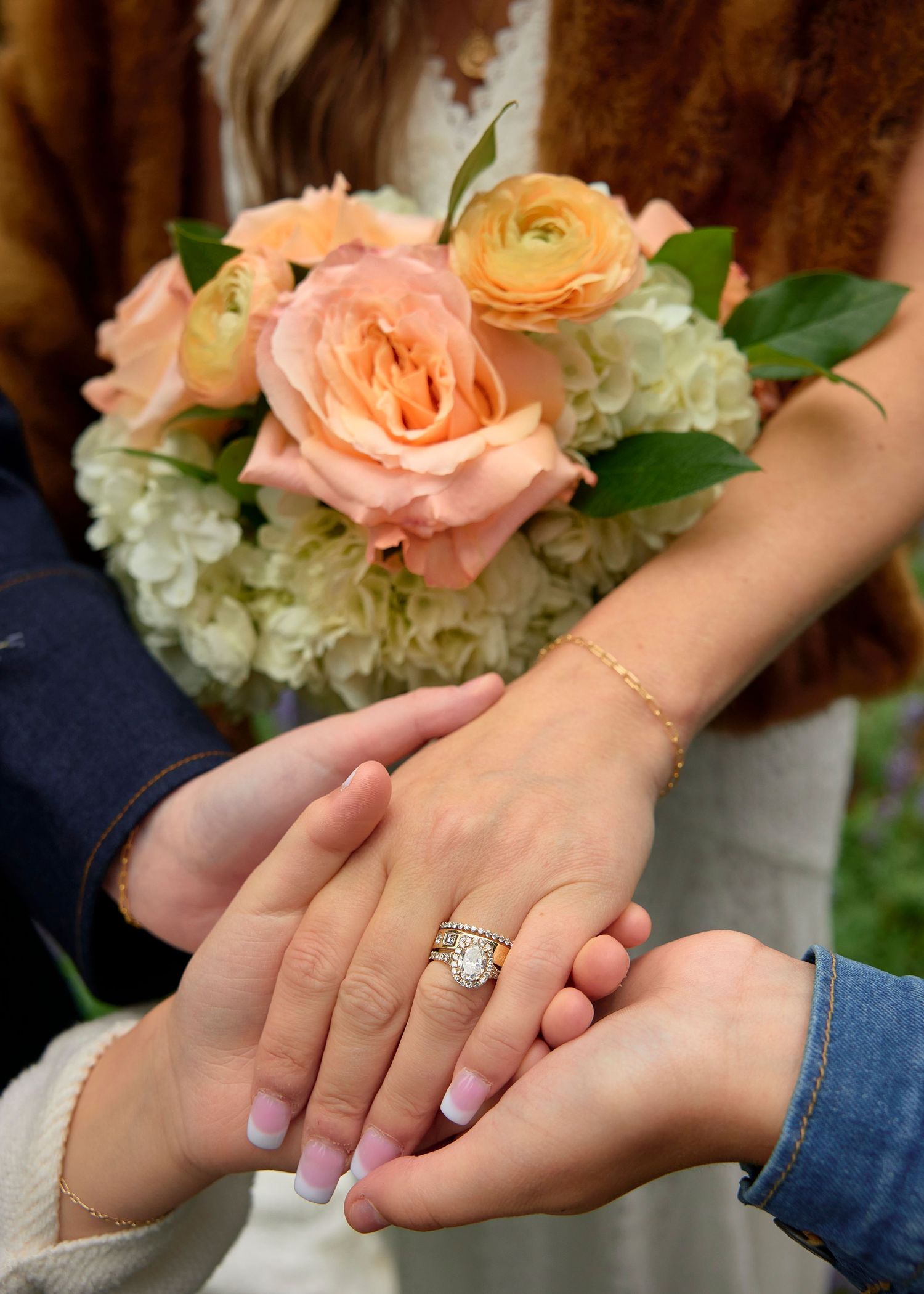 Close-up of bride and groom holding hands showing diamond engagement ring with peach rose bouquet.