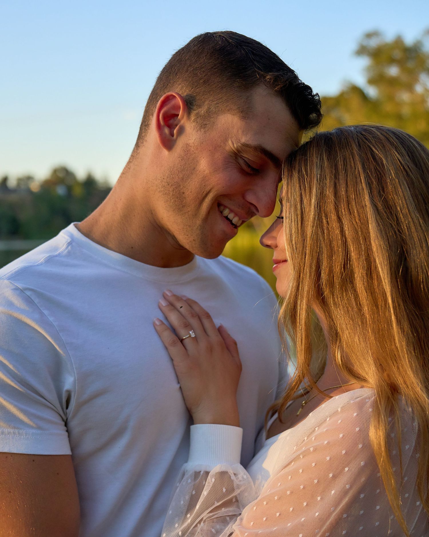 Smiling couple touching foreheads during golden hour outdoor engagement photo session.