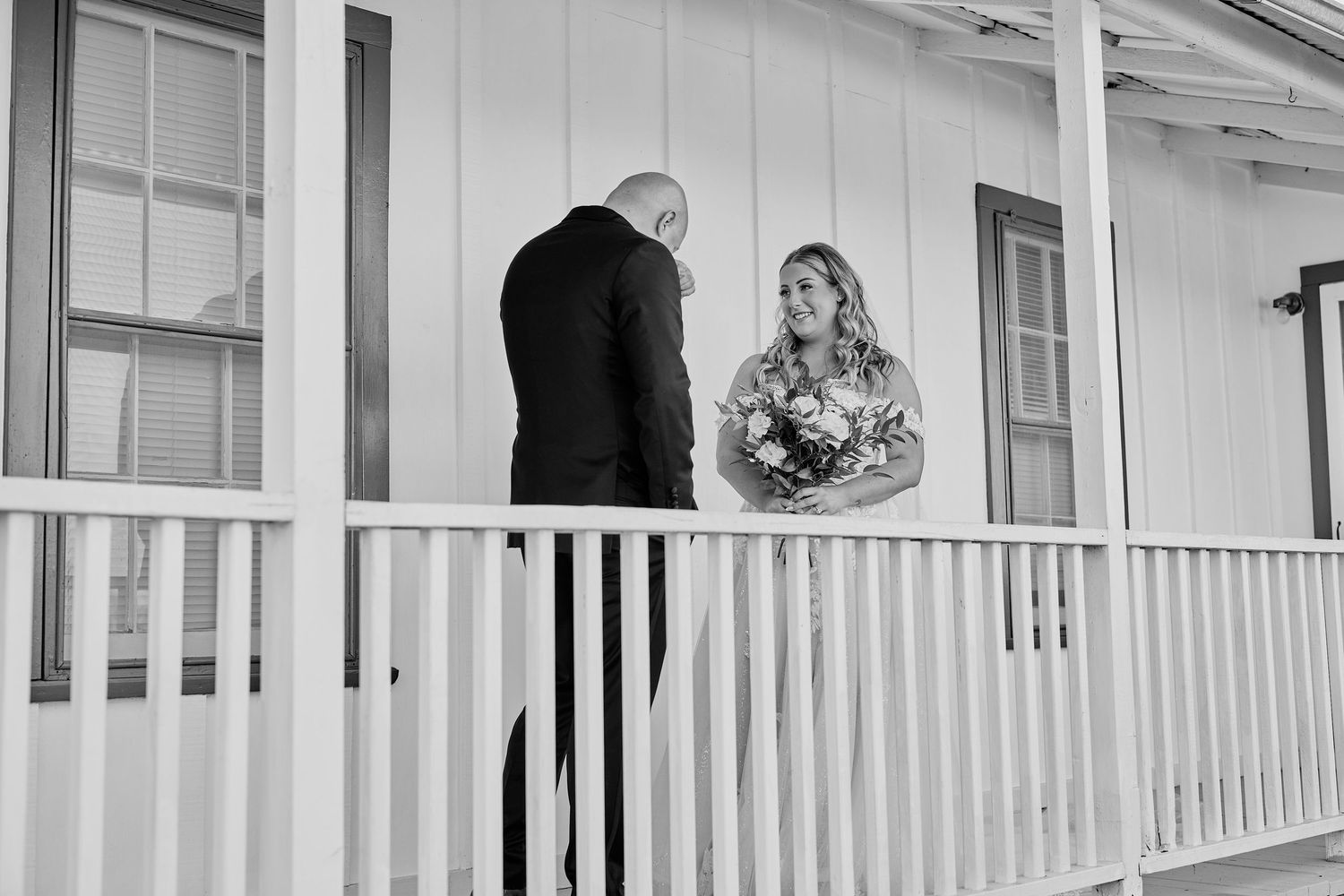 Black and white photo of bride and groom sharing a quiet moment on a white porch railing.