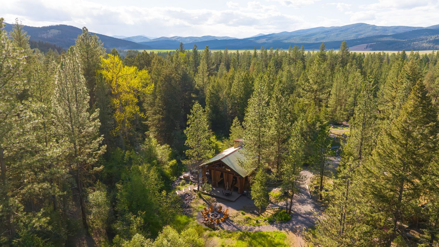 Aerial view of a secluded log cabin nestled among dense pine trees with mountain views.
