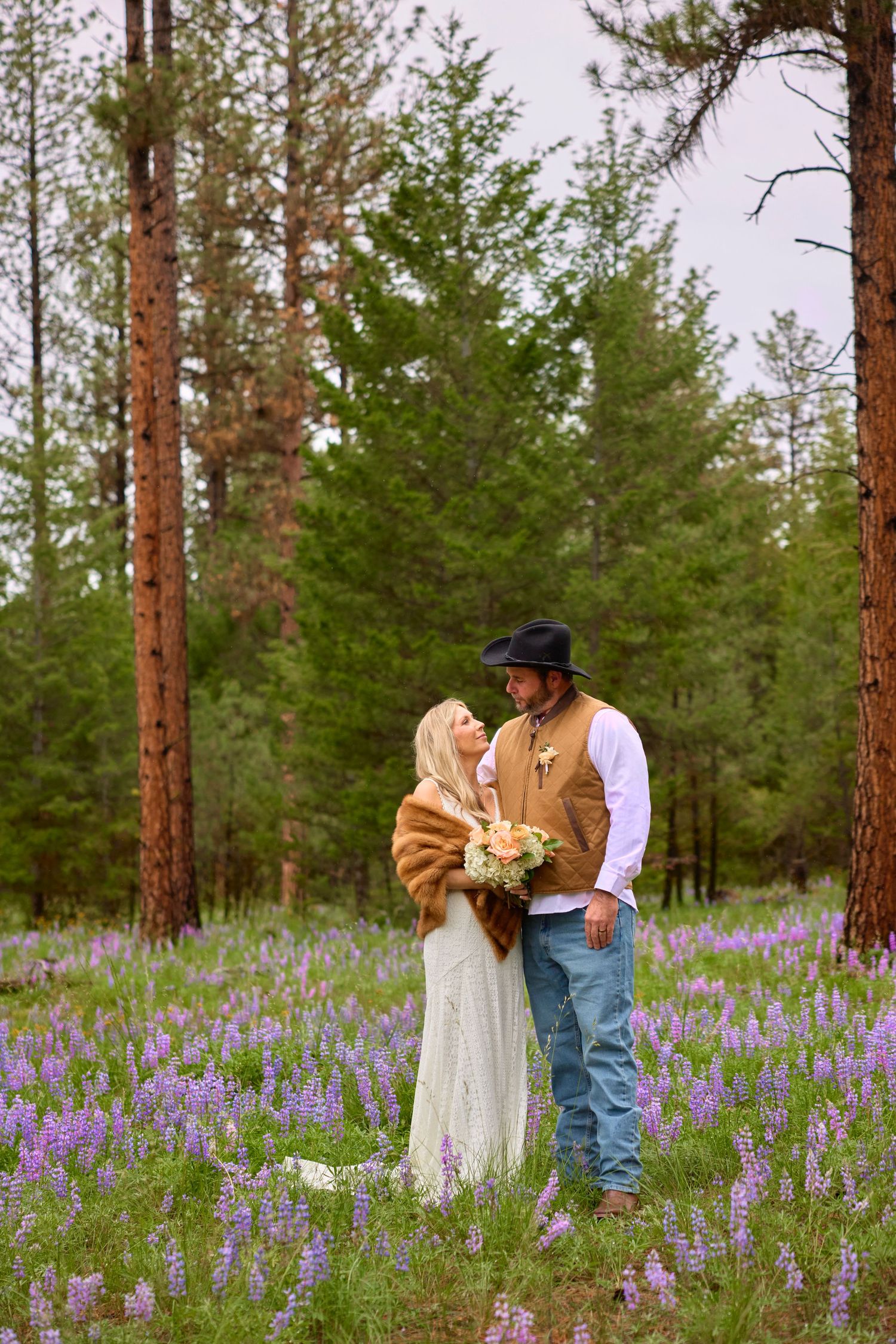Bride and groom share a romantic moment in a purple lupine forest meadow.