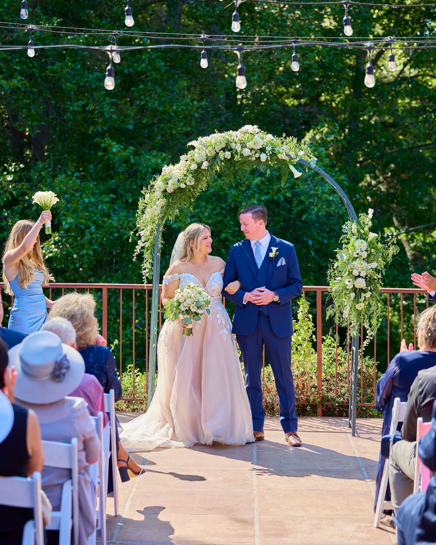 Bride and groom walking down aisle under floral arch at outdoor wedding ceremony.
