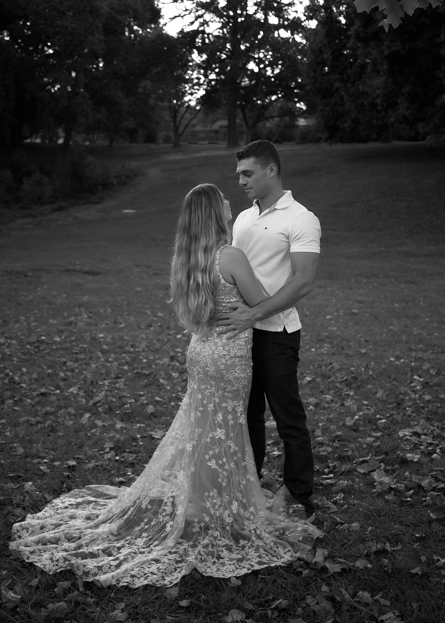 Couple embracing in black and white photo, woman in lace gown, man in white shirt outdoors.