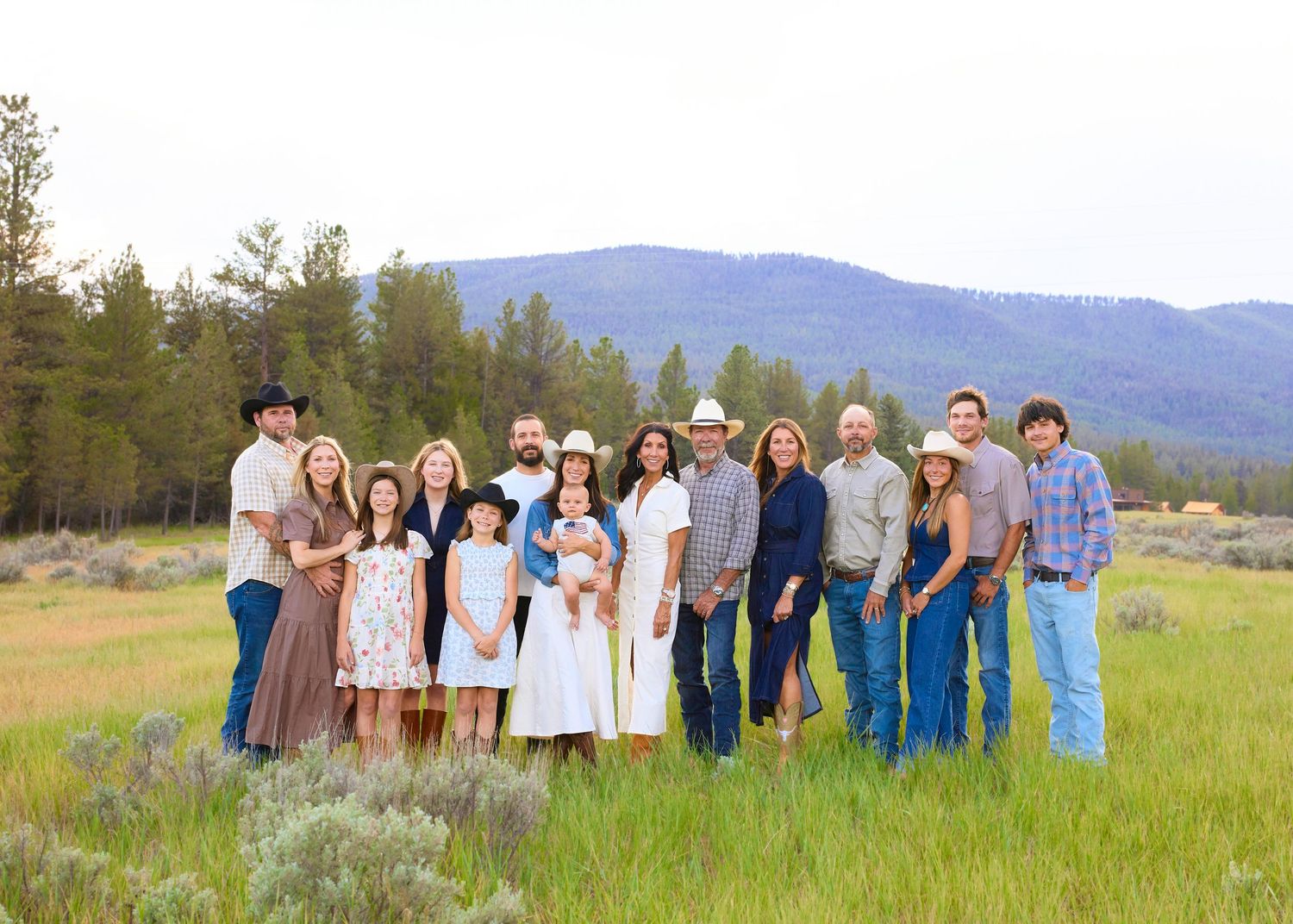 Large family portrait in a scenic mountain meadow with sagebrush, posing together in western-style attire at golden hour.