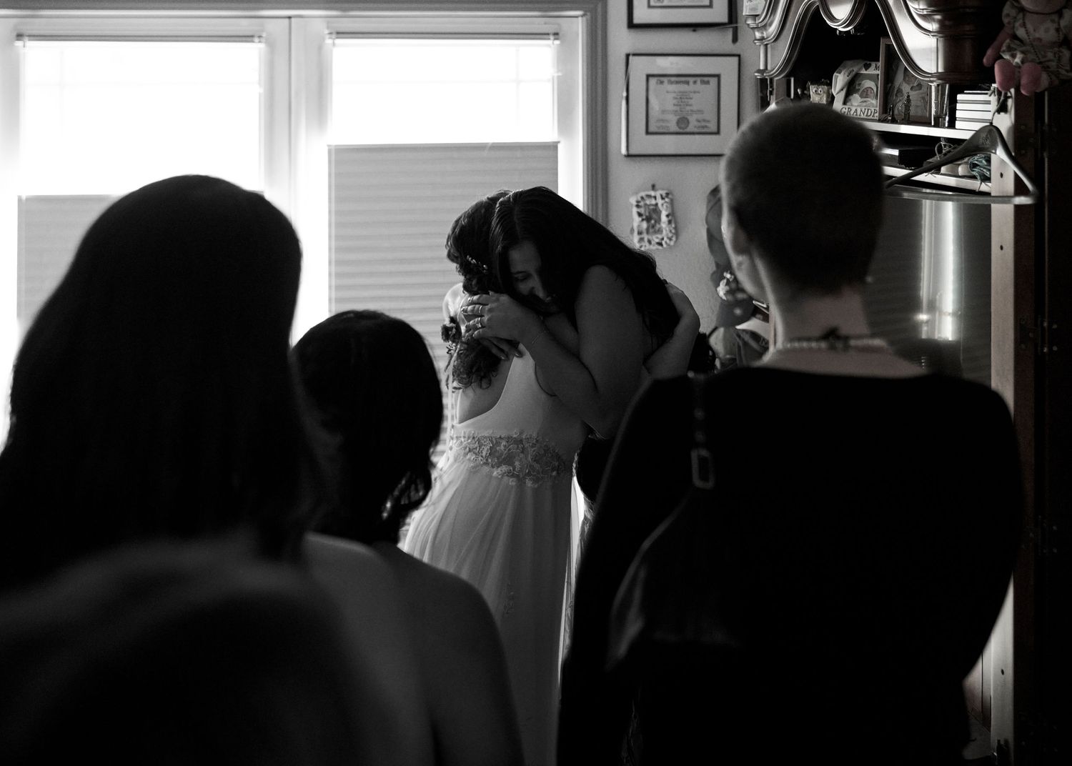 Black and white image of bride in wedding dress sharing an emotional moment with loved ones by a window.
