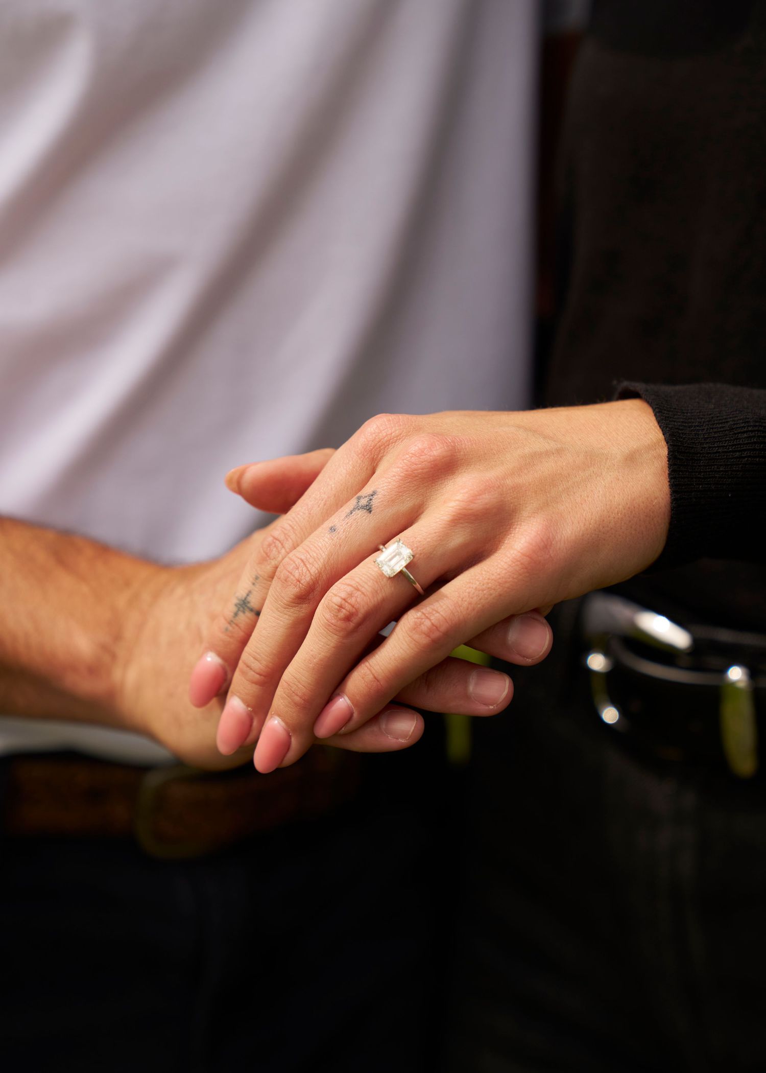 Close-up of couple holding hands showing a square diamond engagement ring and small hand tattoos near a horse.