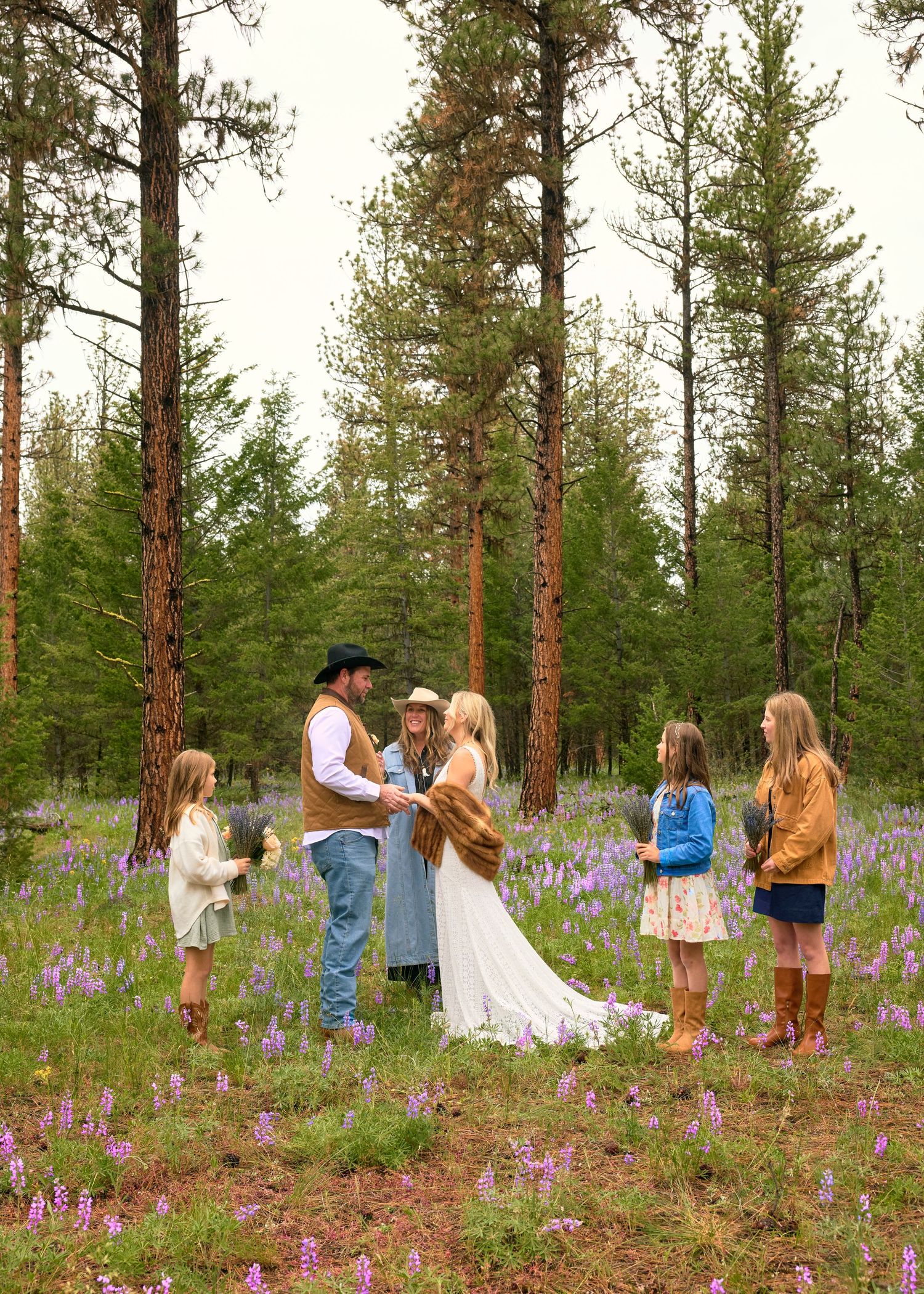 Rustic outdoor wedding ceremony in a wildflower meadow surrounded by pine trees with children as witnesses.