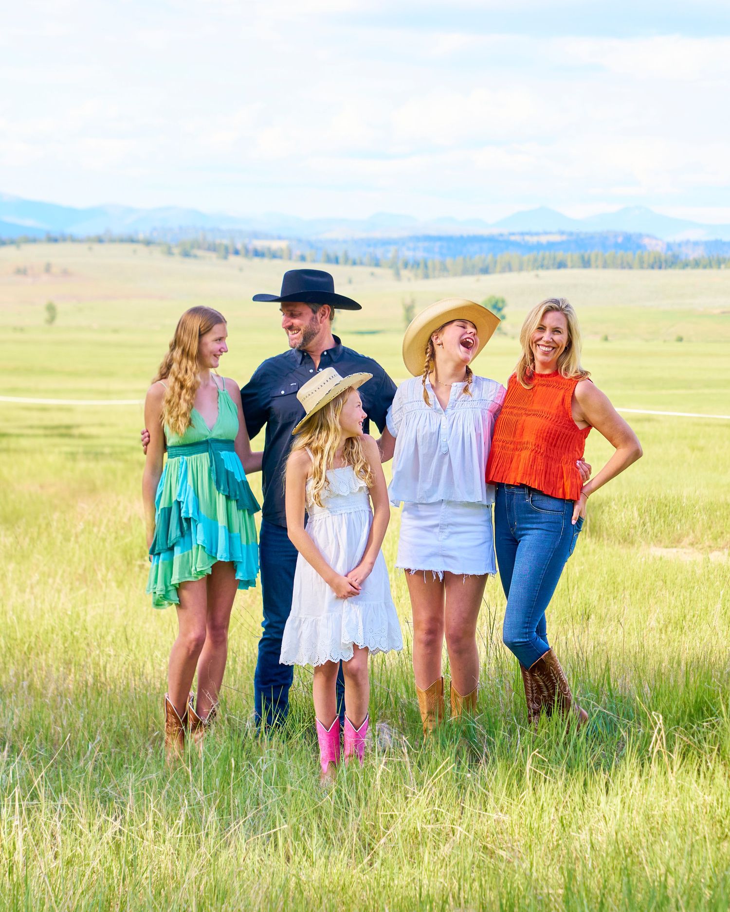 Joyful family of five in western attire laughing together in a scenic green meadow.