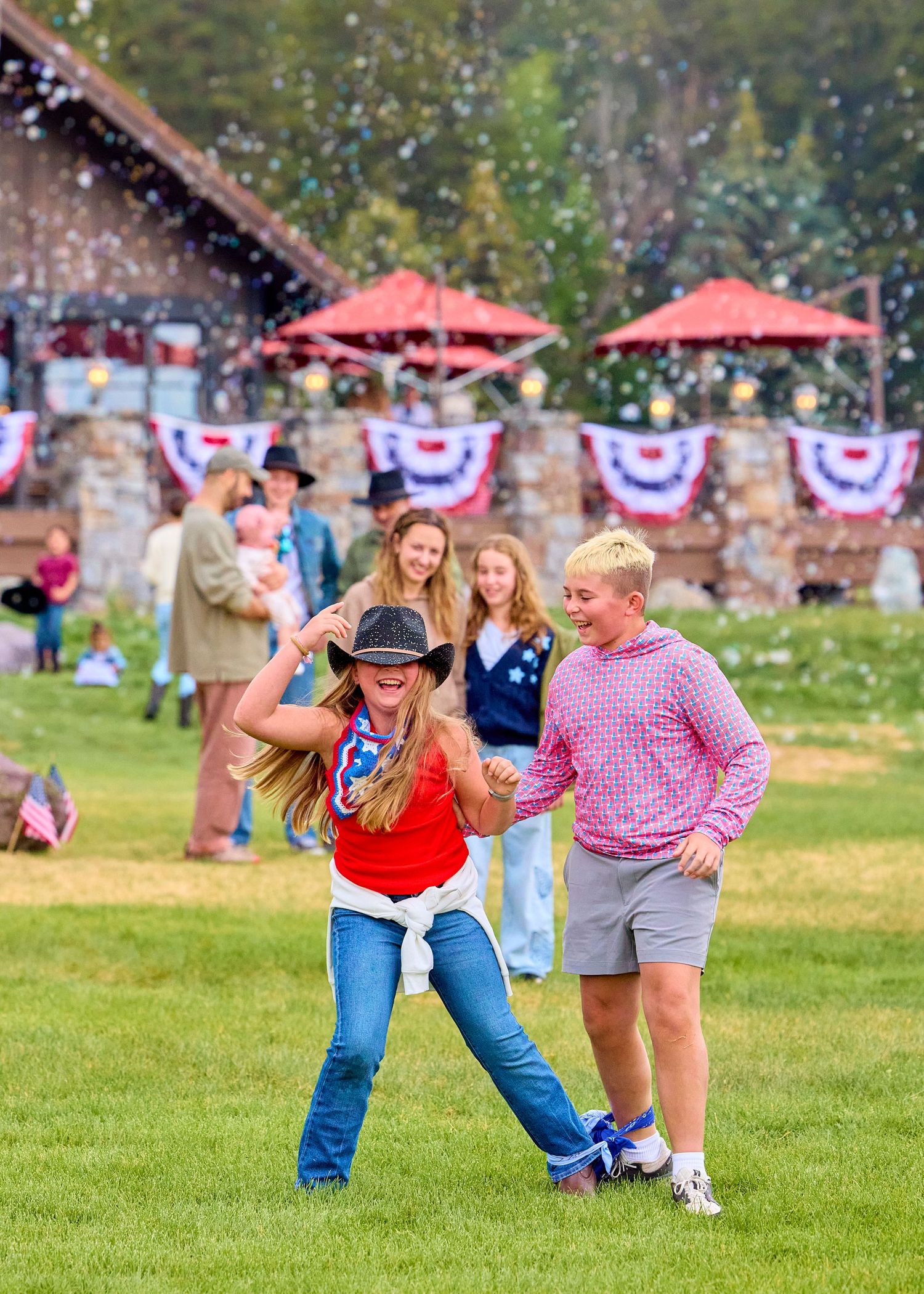 Two women dancing on grass at a patriotic outdoor celebration with festive bunting in background.