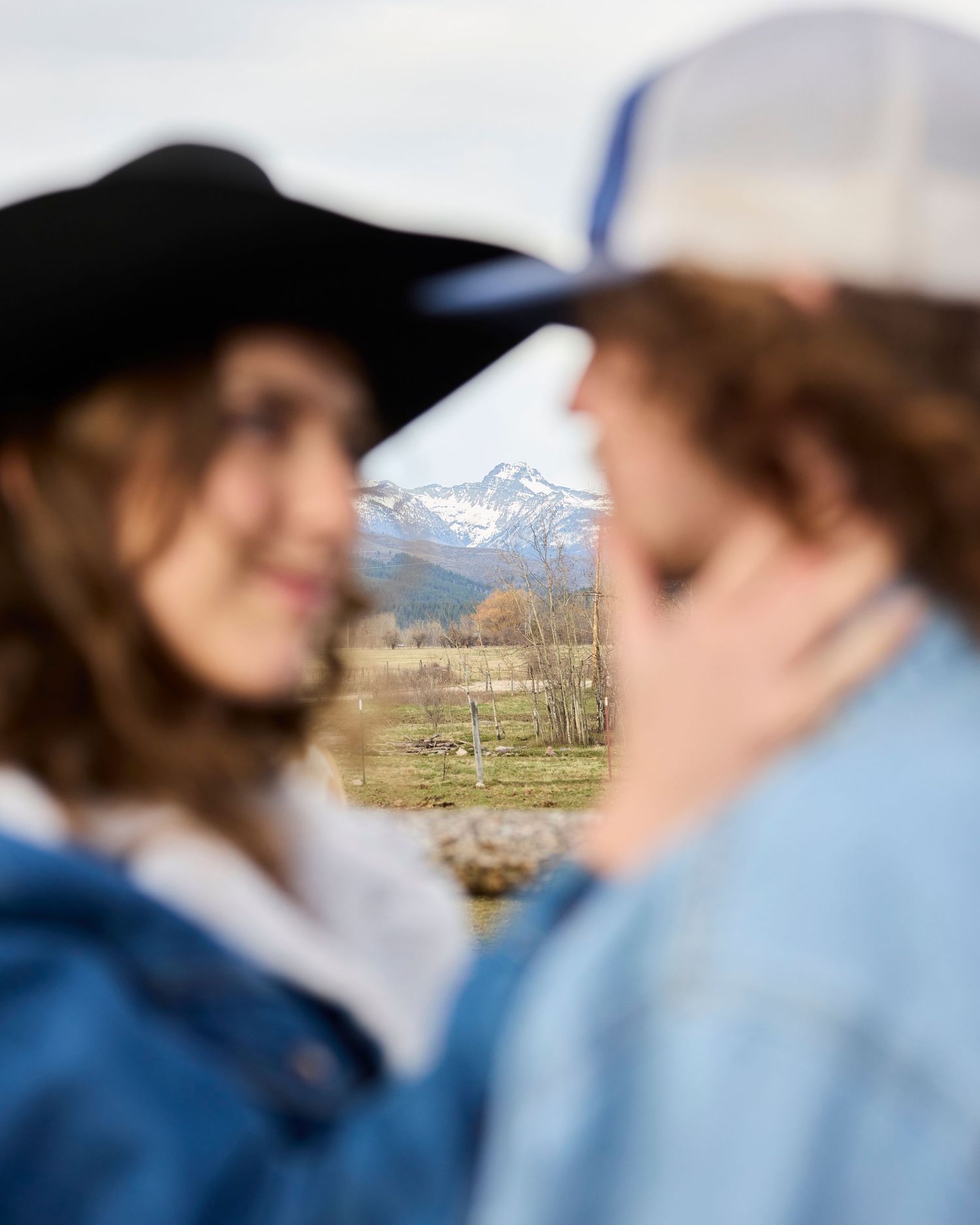 Blurred couple in denim jackets facing each other with snow-capped mountain in focus.