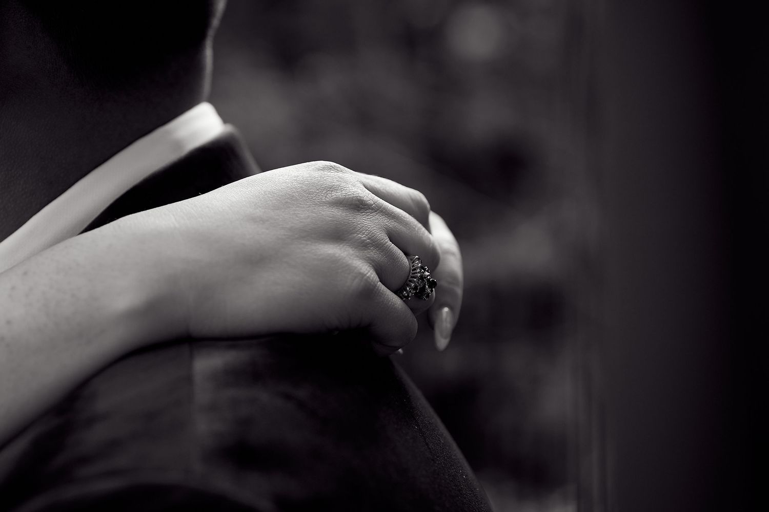 A close-up black and white photo of a bride resting her hand on the groom's shoulder wearing a ring.