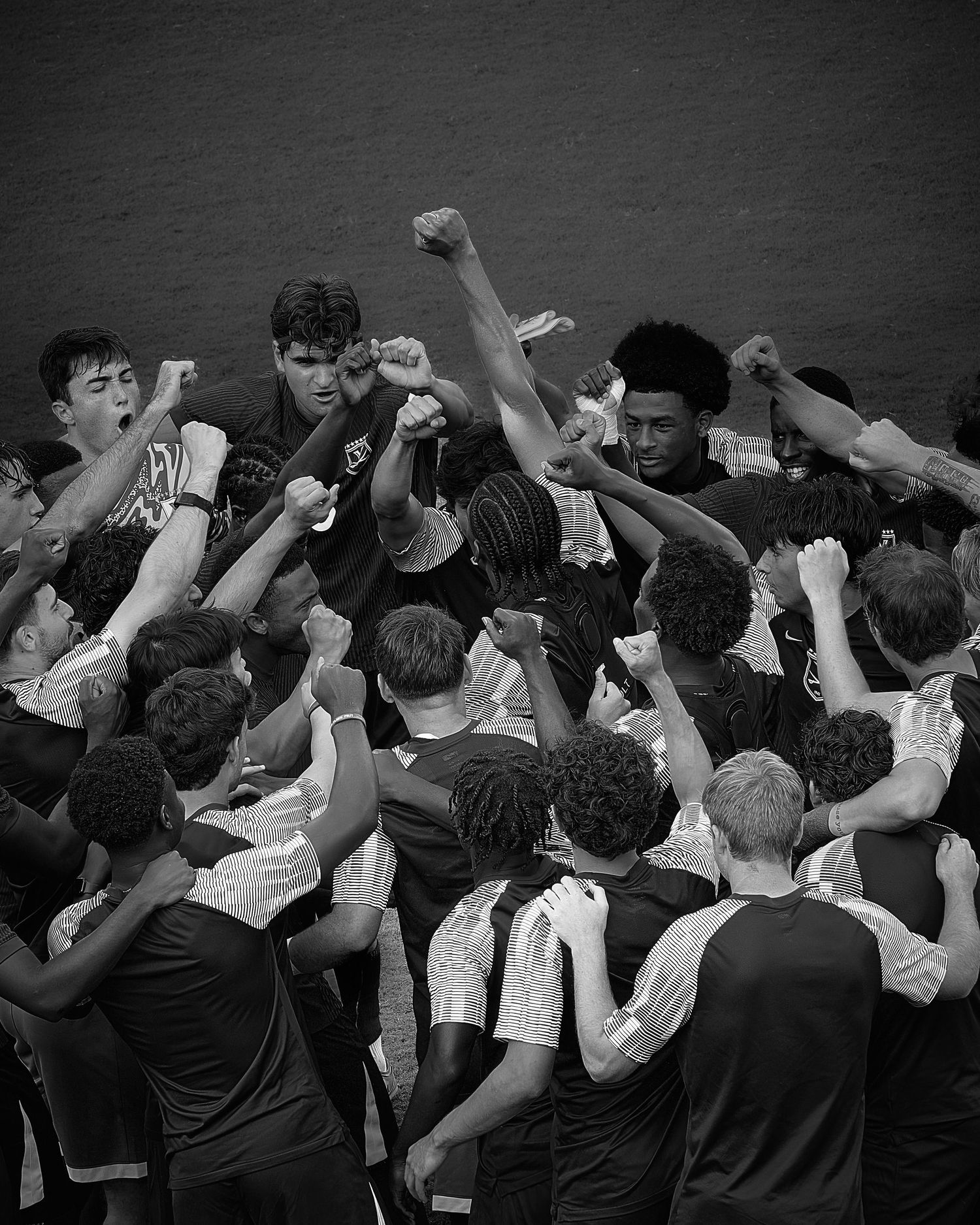 Black and white photo of a diverse youth sports team huddling together with raised fists in a show of unity.