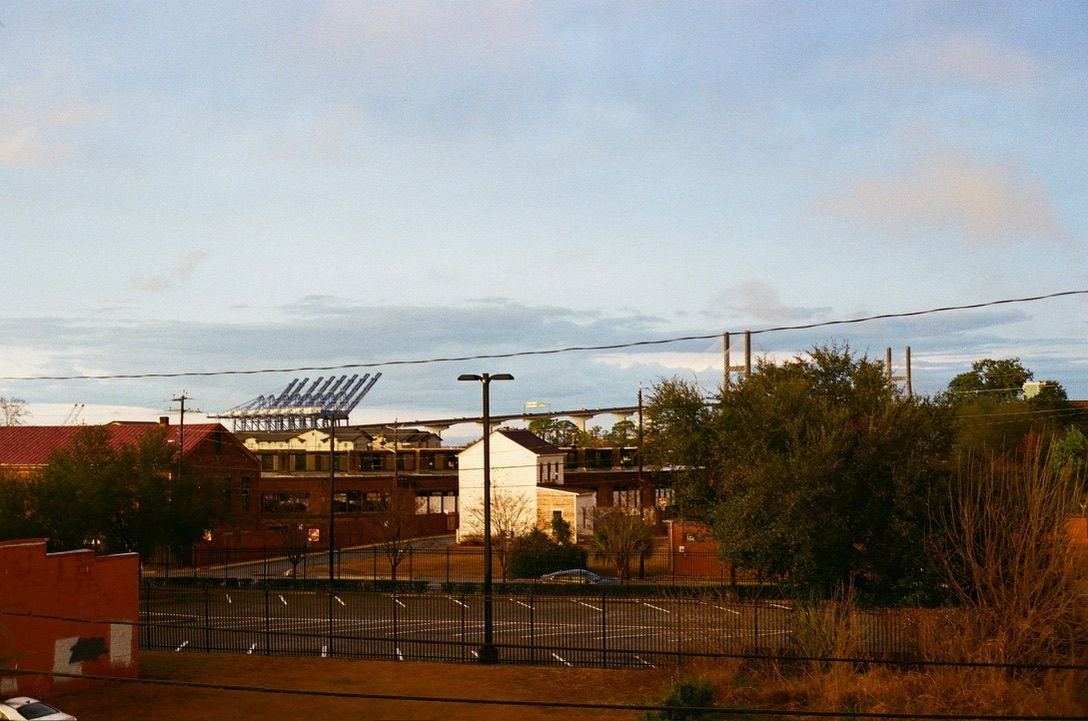 Urban skyline with solar panels on brick building, power lines, trees, and parking lot under partly cloudy sky.