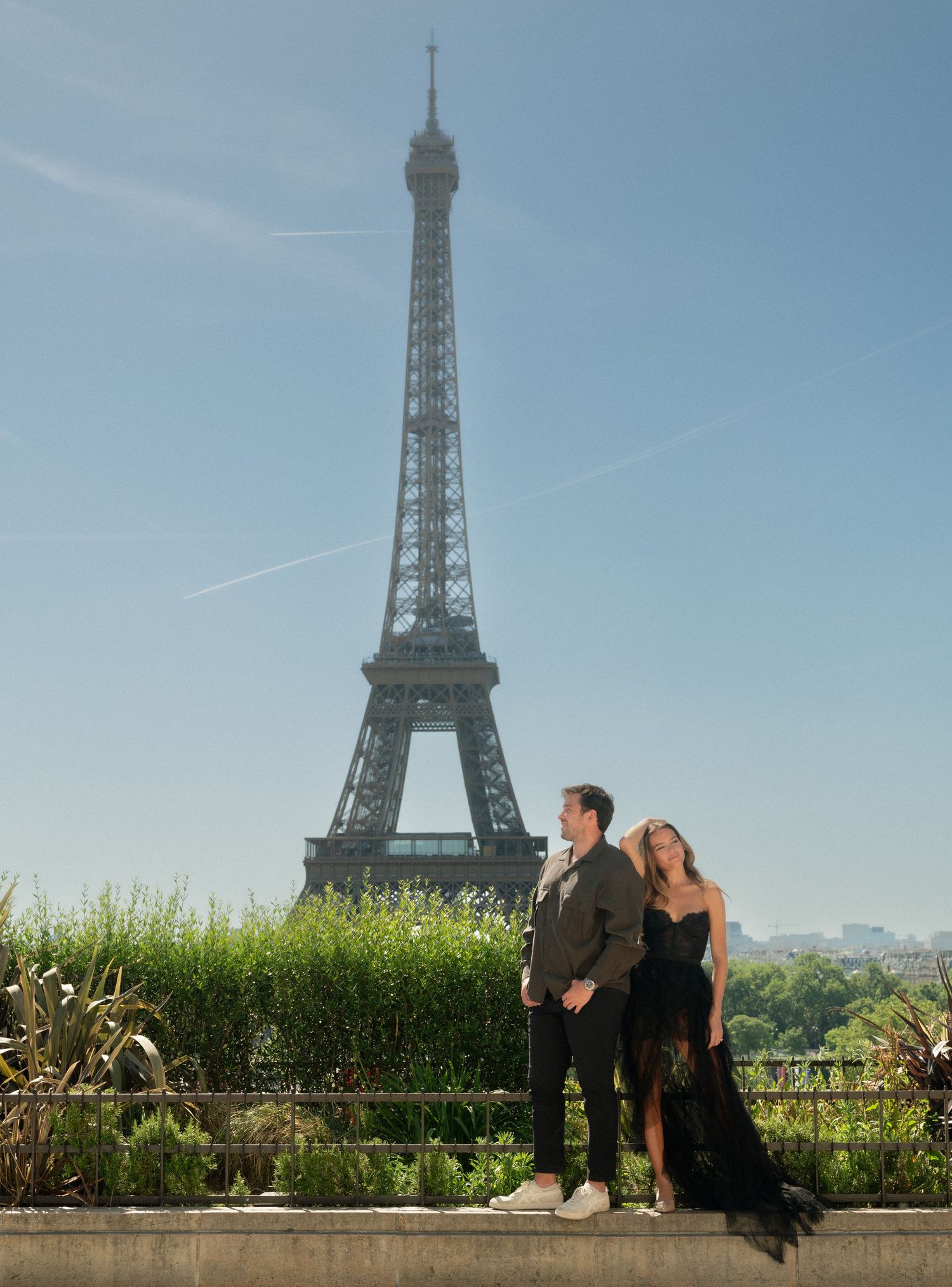 Couple embracing with the iconic Eiffel Tower rising behind them under a clear blue sky in Paris.