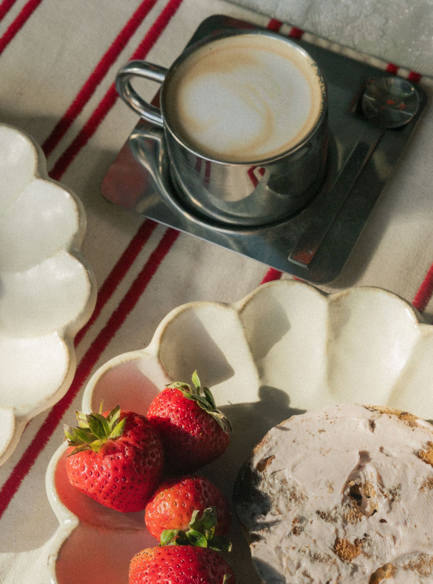 Overhead view of a cappuccino, fresh strawberries, and rustic bread on white ceramic dishes with a striped linen cloth.