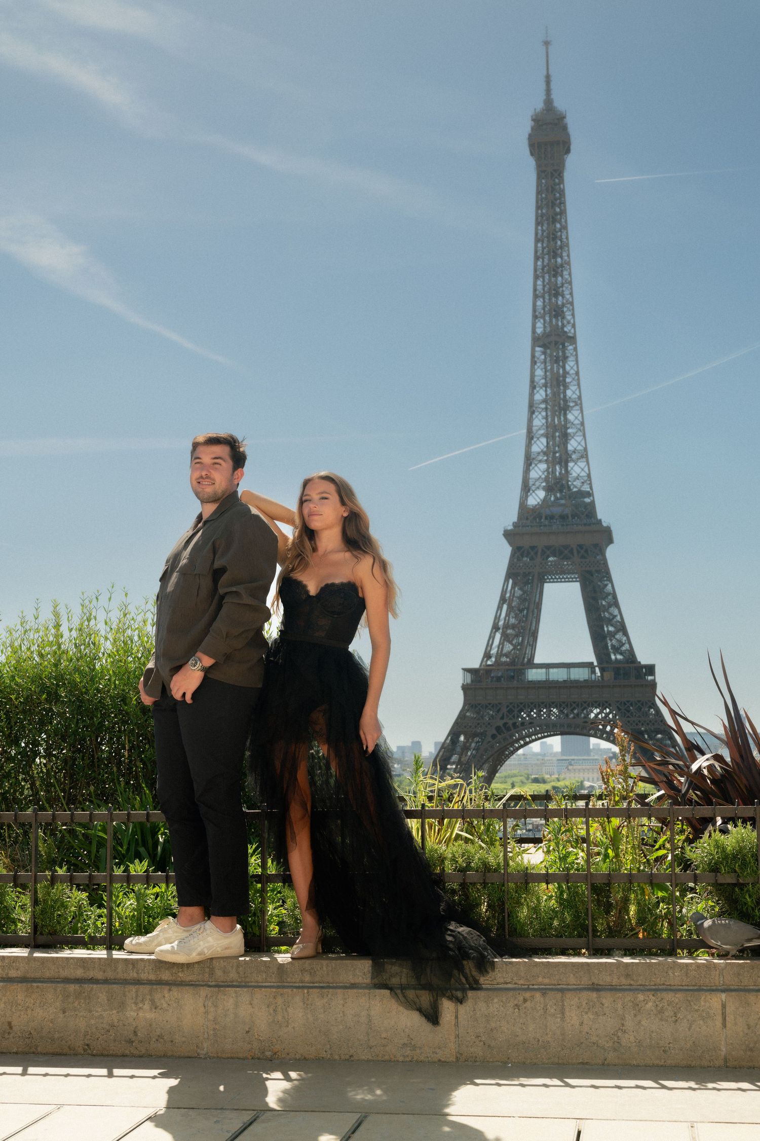 Stylish couple poses before the Eiffel Tower on a sunny day in Paris.