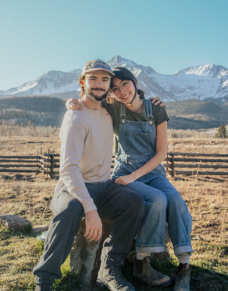 Smiling couple sitting together with snow-capped Rocky Mountains in background.