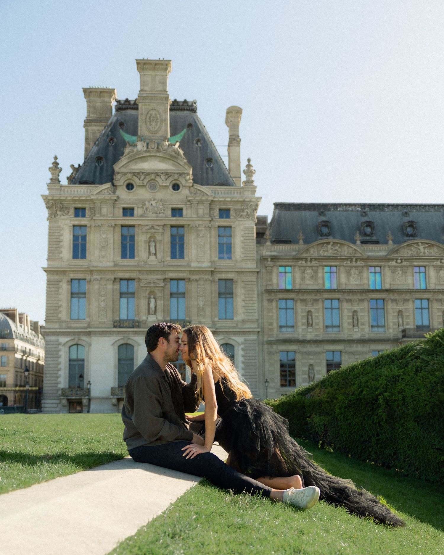 Couple kisses on grass in front of the Louvre museum in Paris.