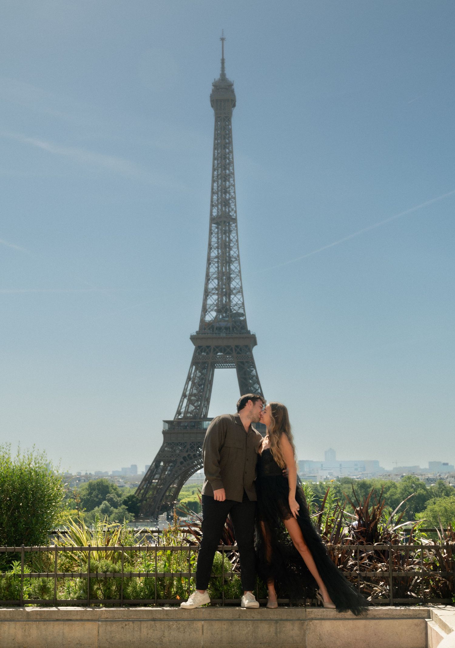 Couple sharing a romantic kiss in front of the Eiffel Tower on a clear sunny day in Paris.