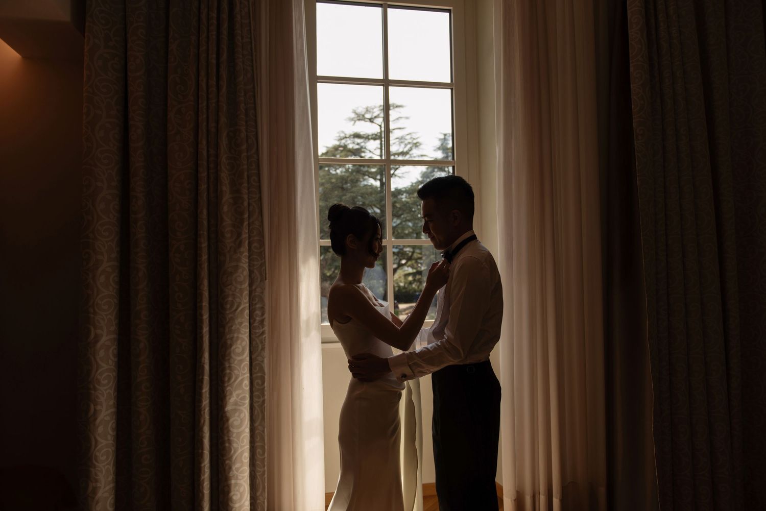 Silhouette of a bride and groom sharing a romantic dance in front of a sunlit window with sheer curtains. Lake Como