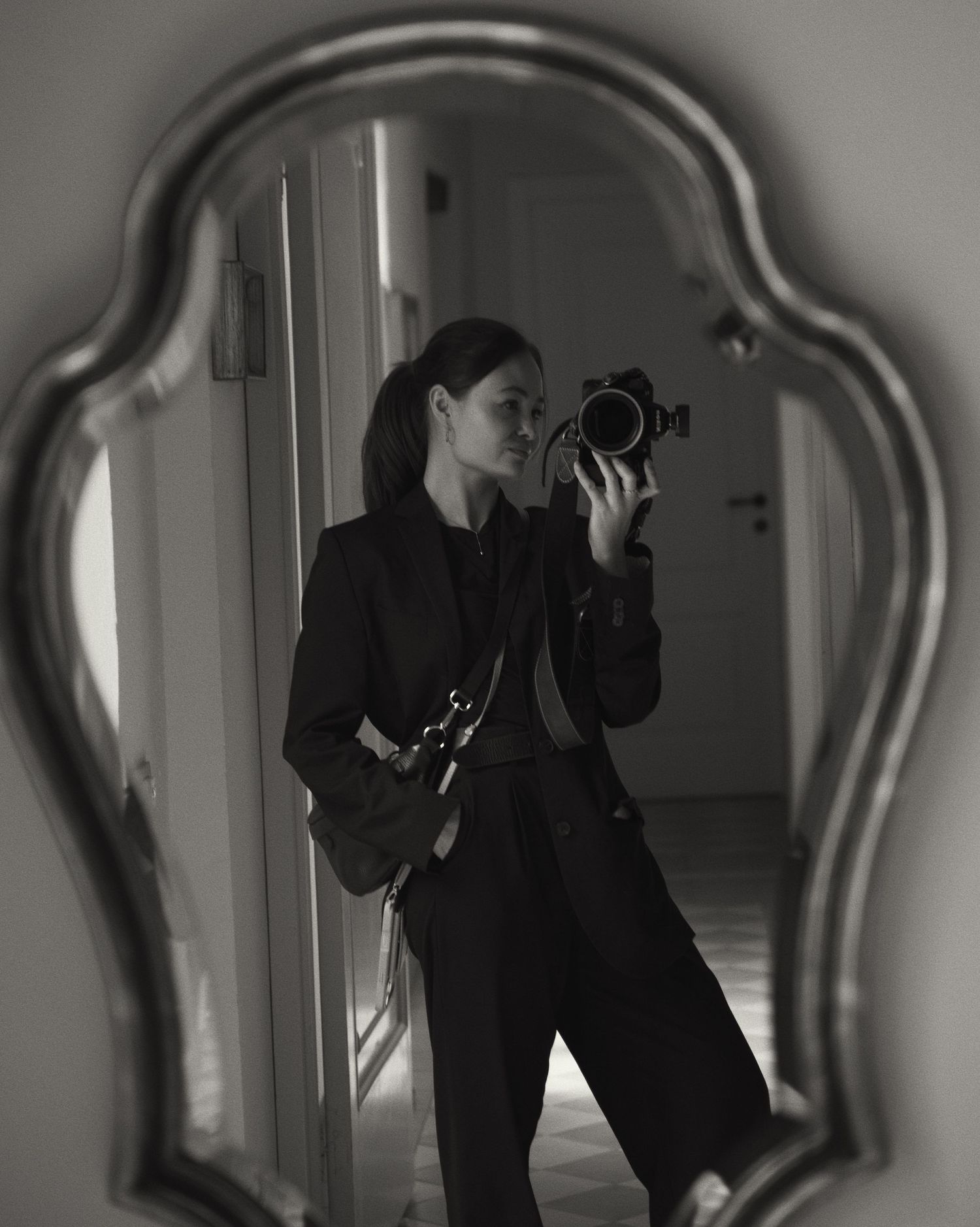 Black and white mirror selfie of a photographer in a black suit holding a professional camera indoors. Lake Como photographer
