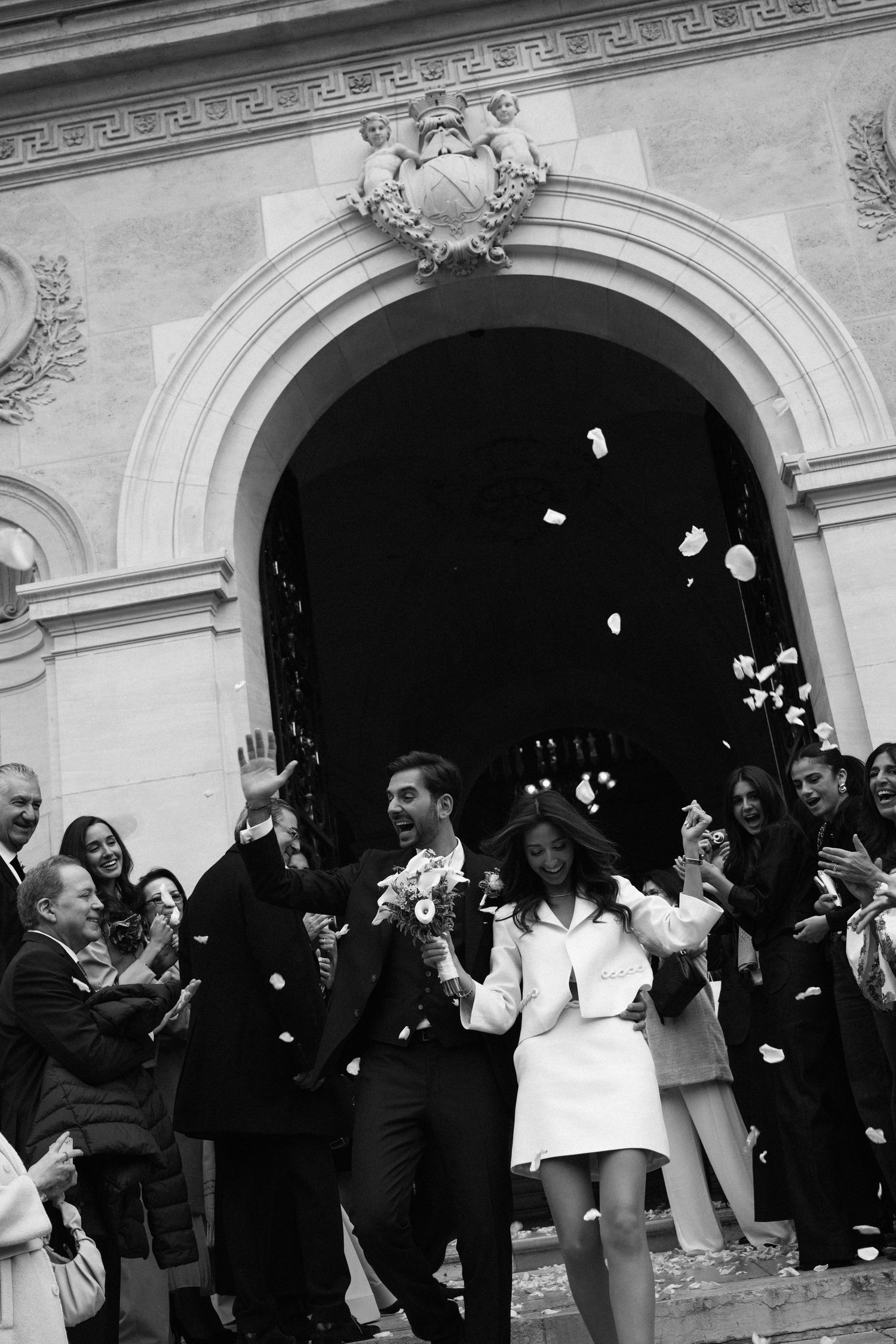 Black and white photo of newlyweds exiting church as guests throw confetti in celebration.