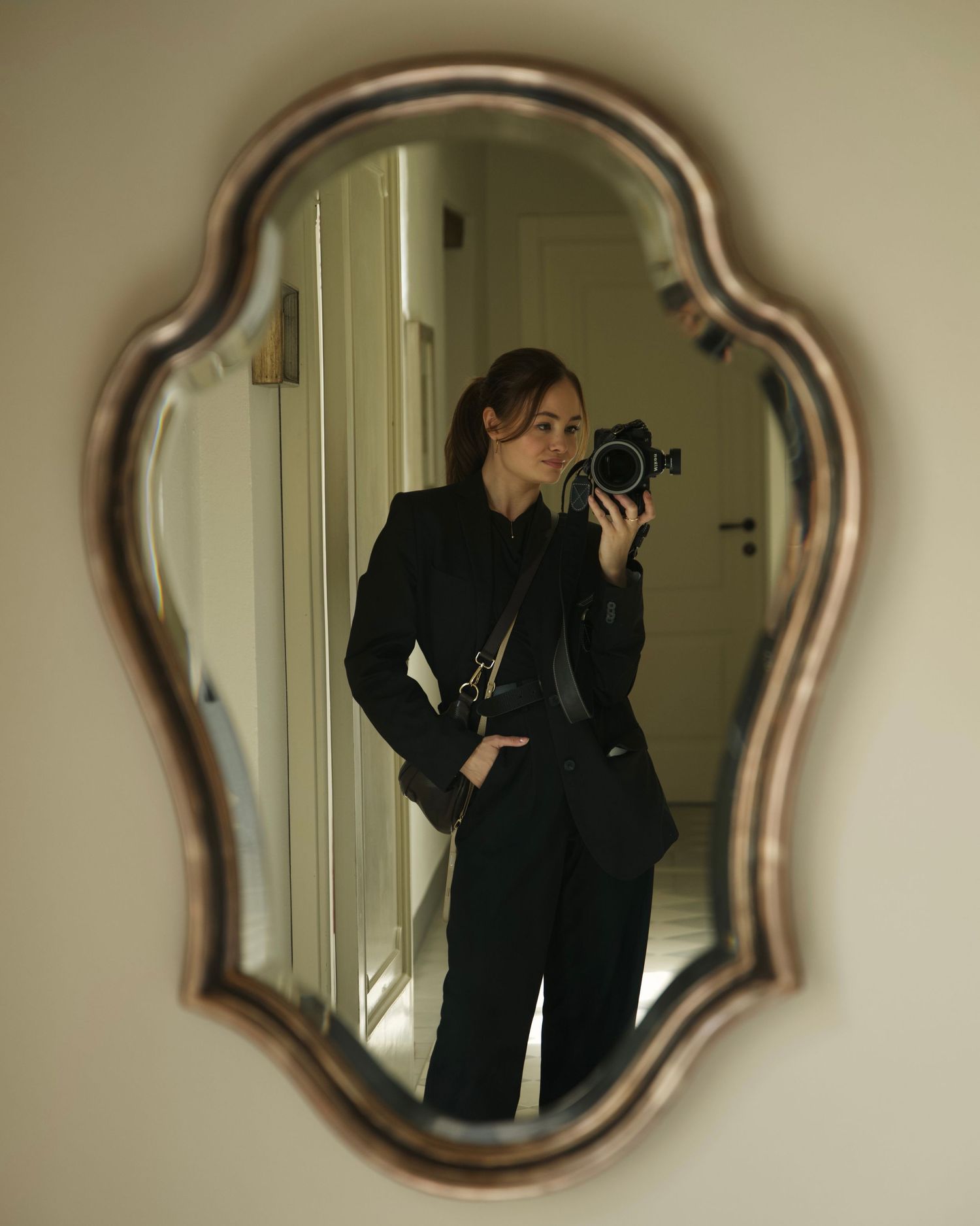 Elegant photographer in all-black attire taking a selfie with a camera in a decorative silver mirror. Lake Como wedding photographer