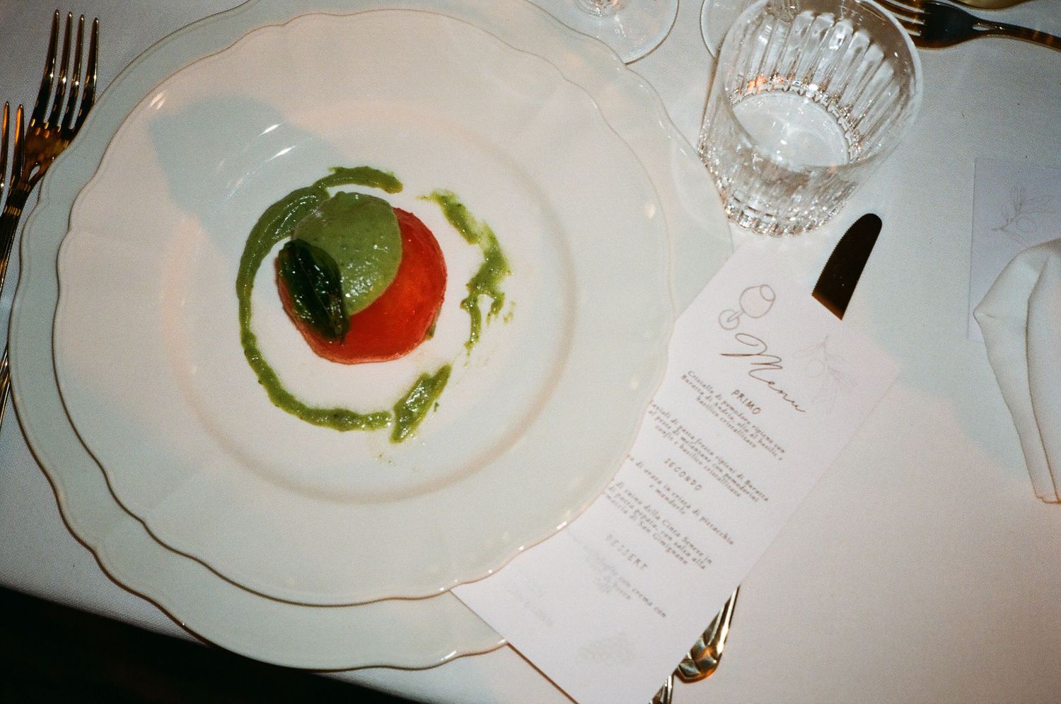 Elegant wedding appetizer of tomato with green pesto sauce on white plate beside printed menu card.