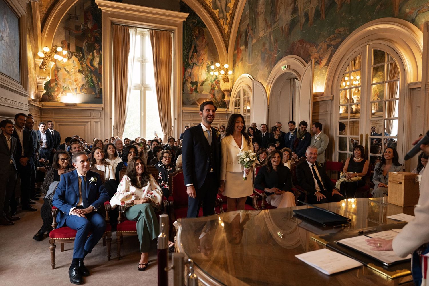 Bride and groom standing at the altar during a civil wedding ceremony in an ornate Parisian town hall.