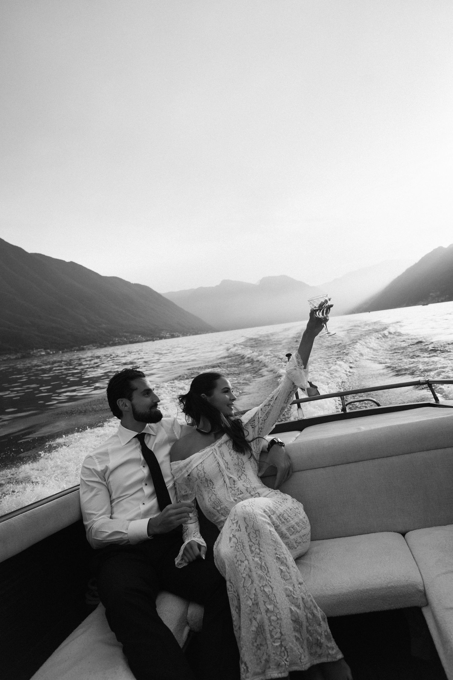 Black and white romantic photo of couple relaxing on boat stern with mountain lake scenery. Lake Como