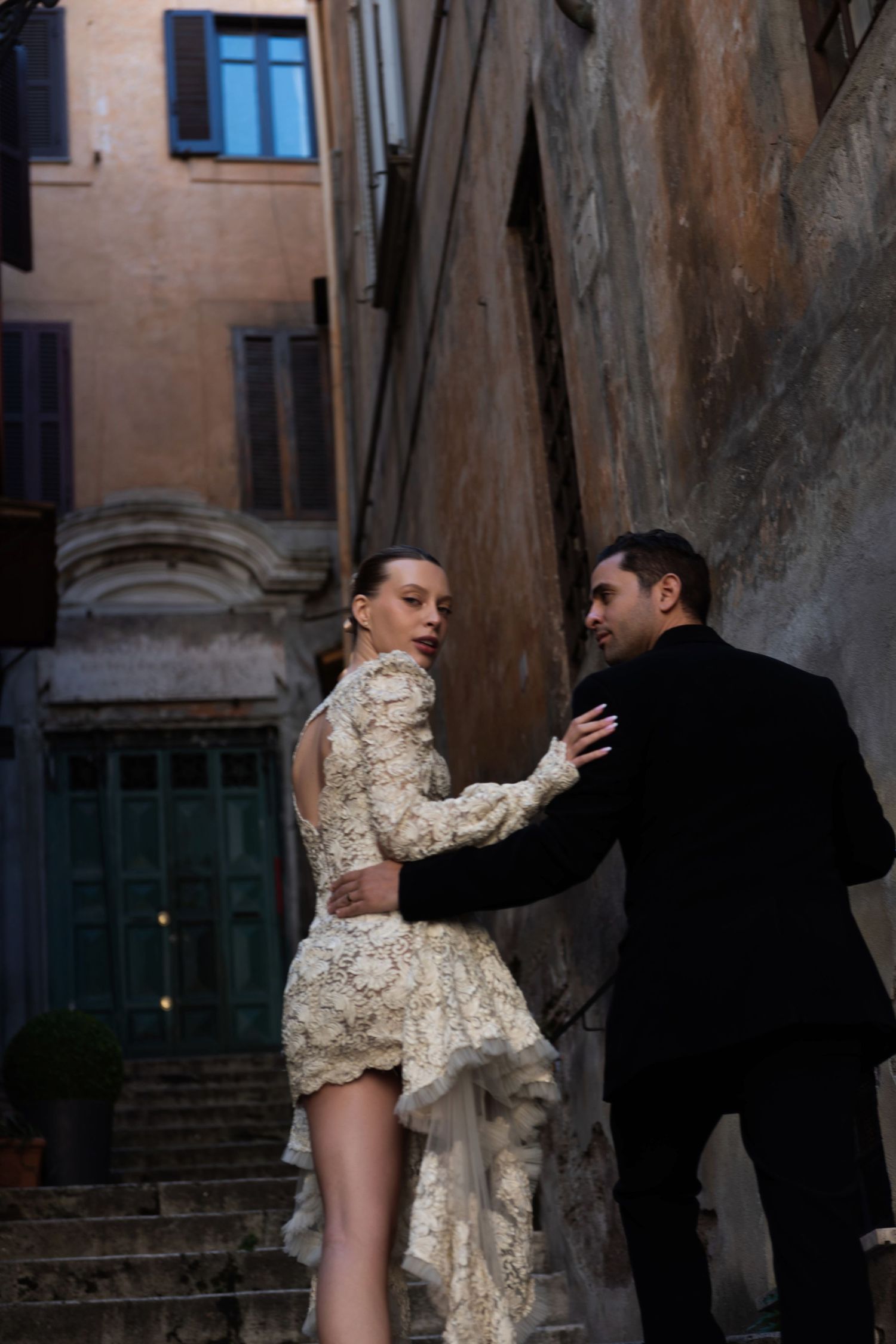 Elegant couple in lace dress and black suit embracing on ancient Rome stone staircase. Roma