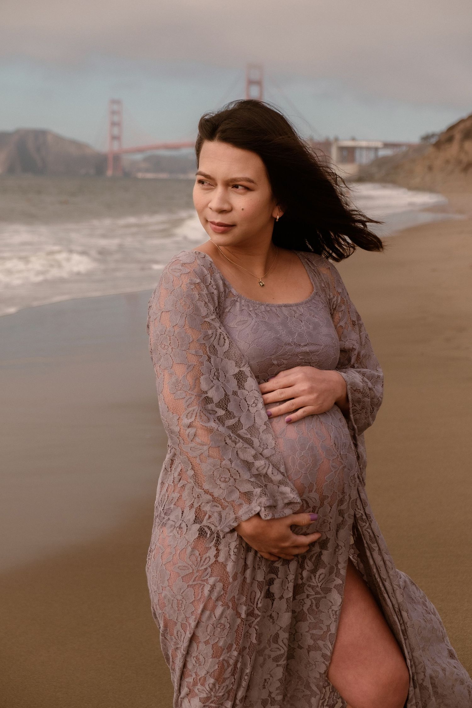 Editorial maternity portrait of a woman in a lace lavender gown on a foggy Bay Area beach