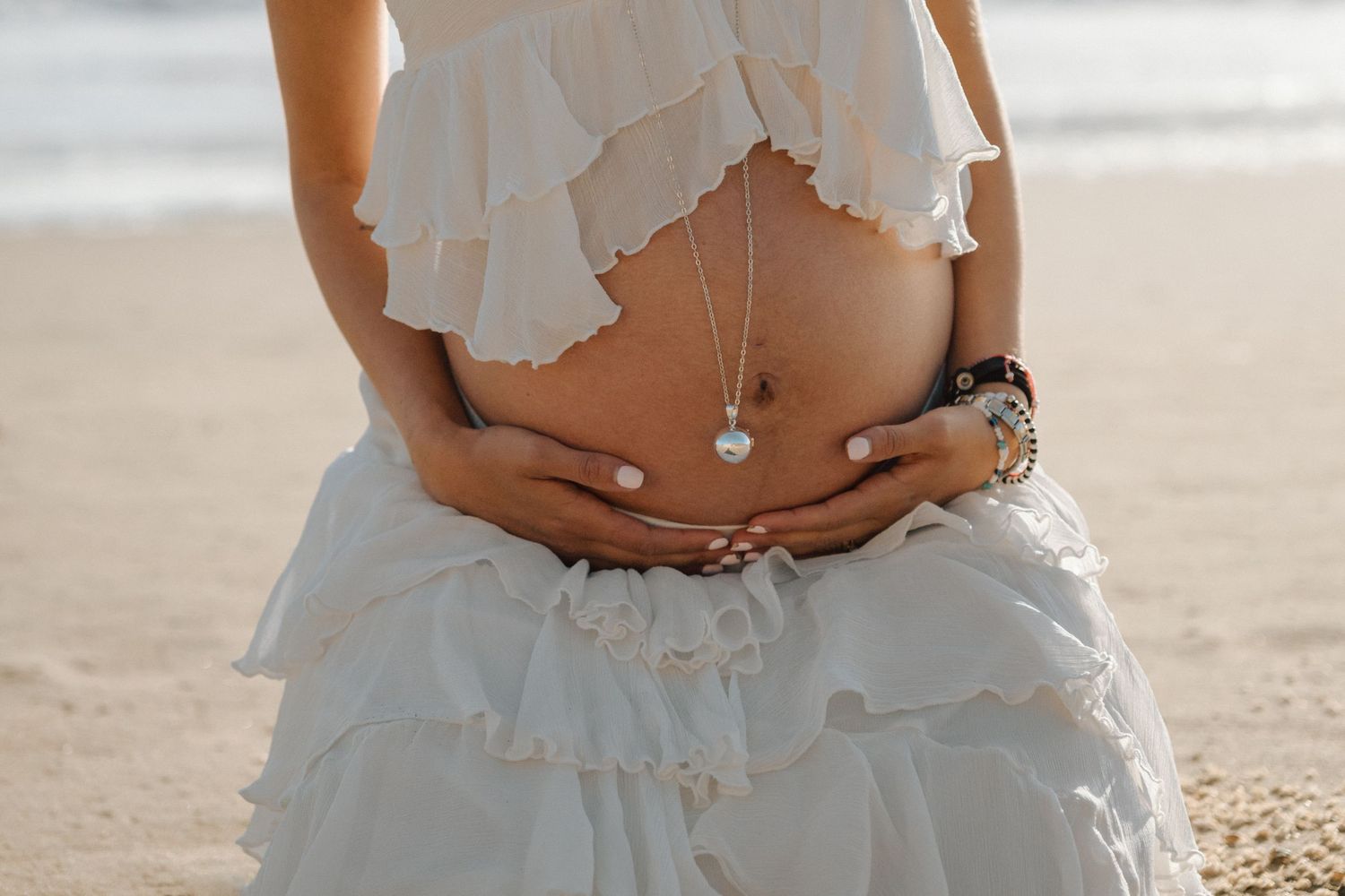 mom holding belly bump with bay area beach background during golden hour maternity photo session in Daly City