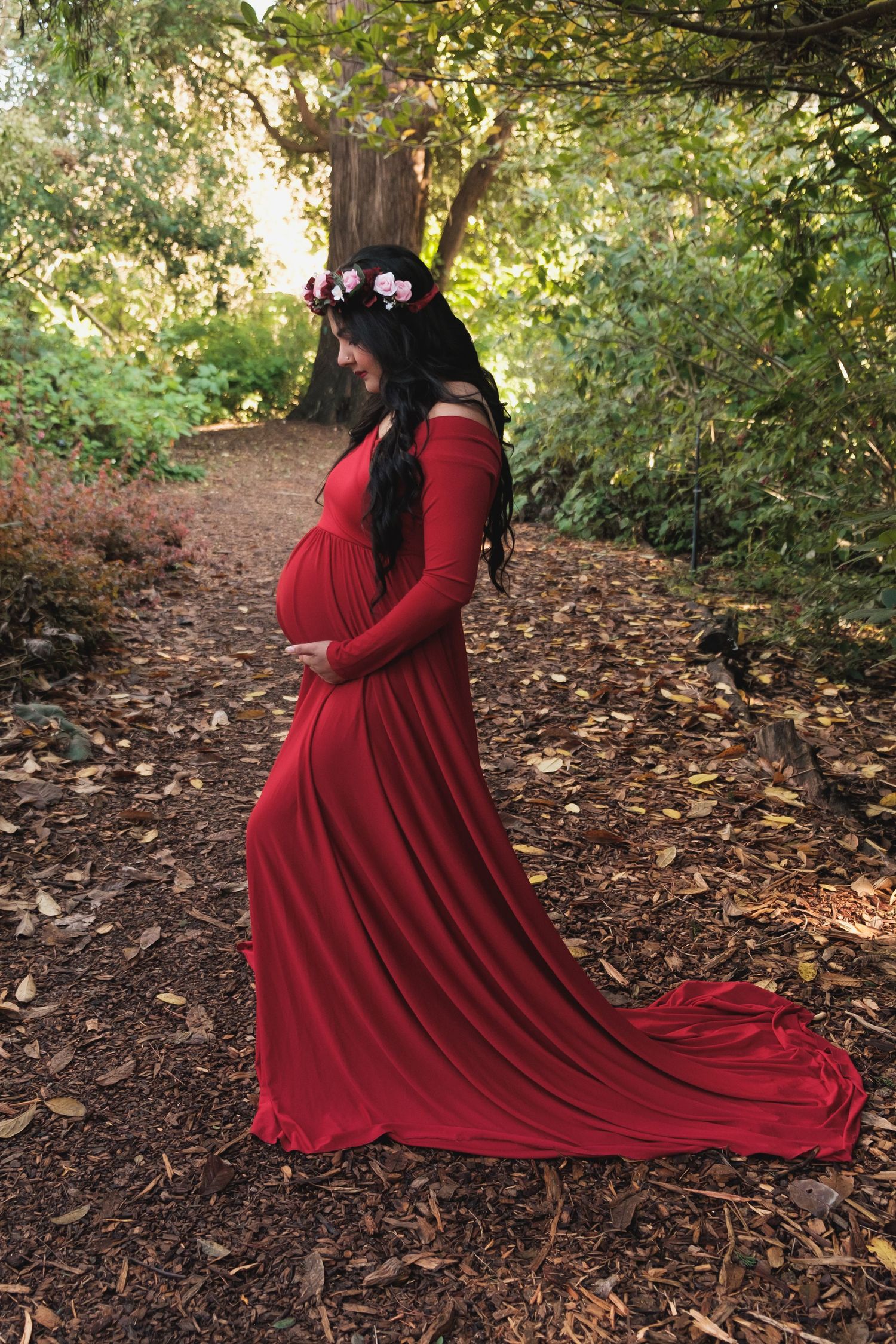 Expectant mother in a flowing red maternity dress posing with her baby bump