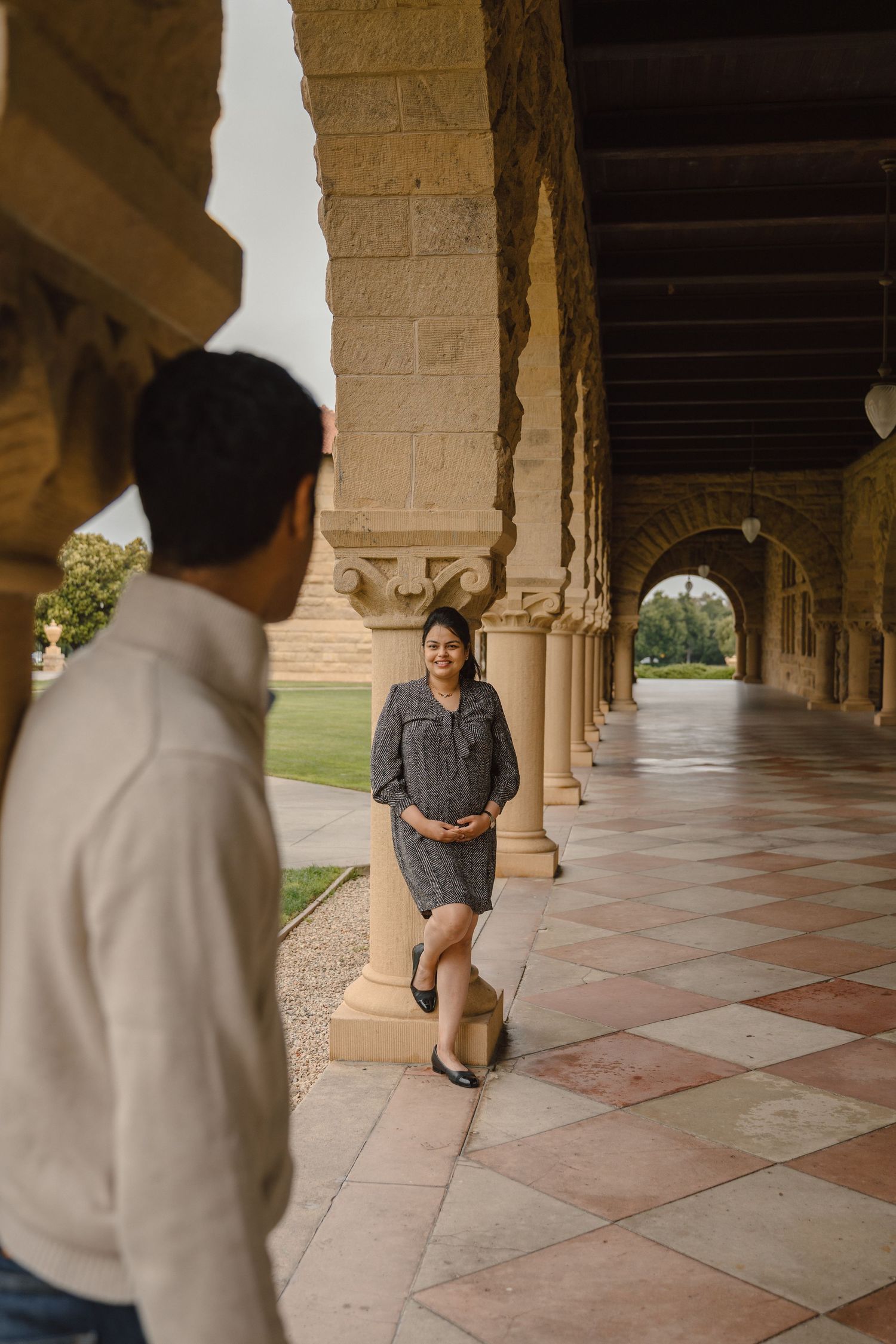 mom to be looking at dad while holding her baby bump in the arches of Stanford University