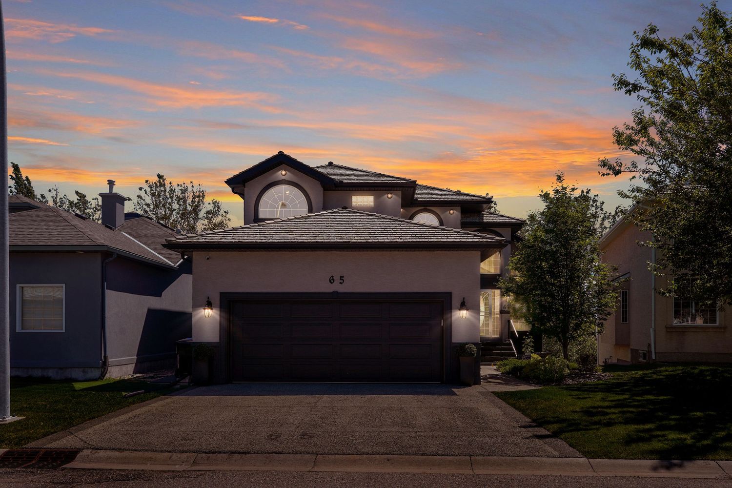 Two-story suburban home with dark garage door glows warmly against a vibrant sunset sky with orange and purple hues.