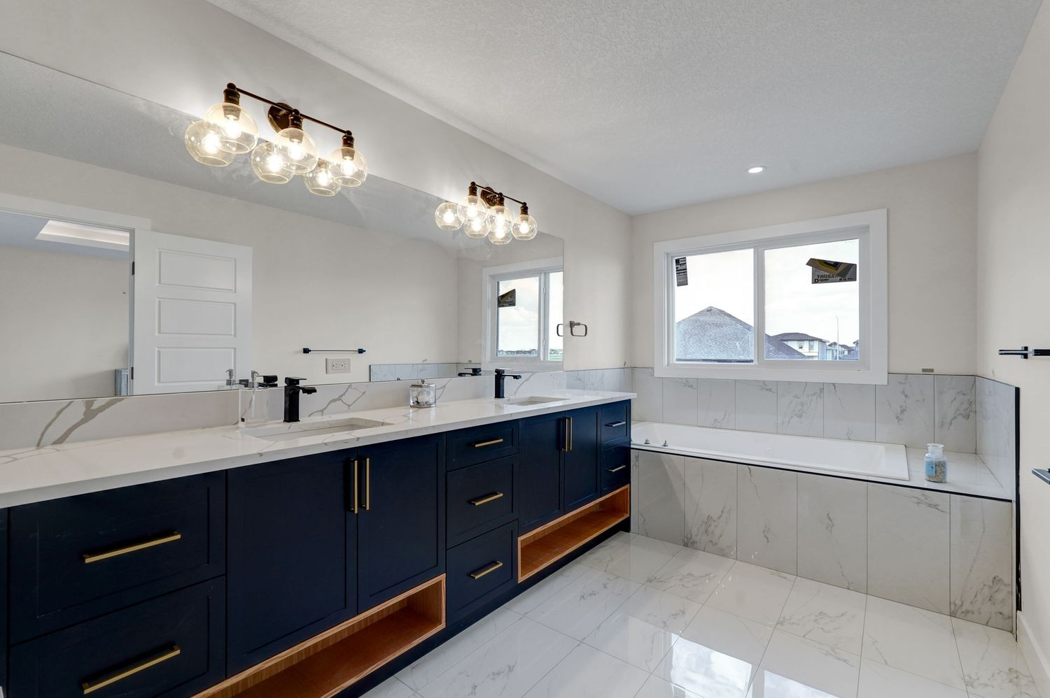 Luxurious bathroom with navy blue cabinetry, white marble countertops, dual sinks, and a freestanding soaking tub.