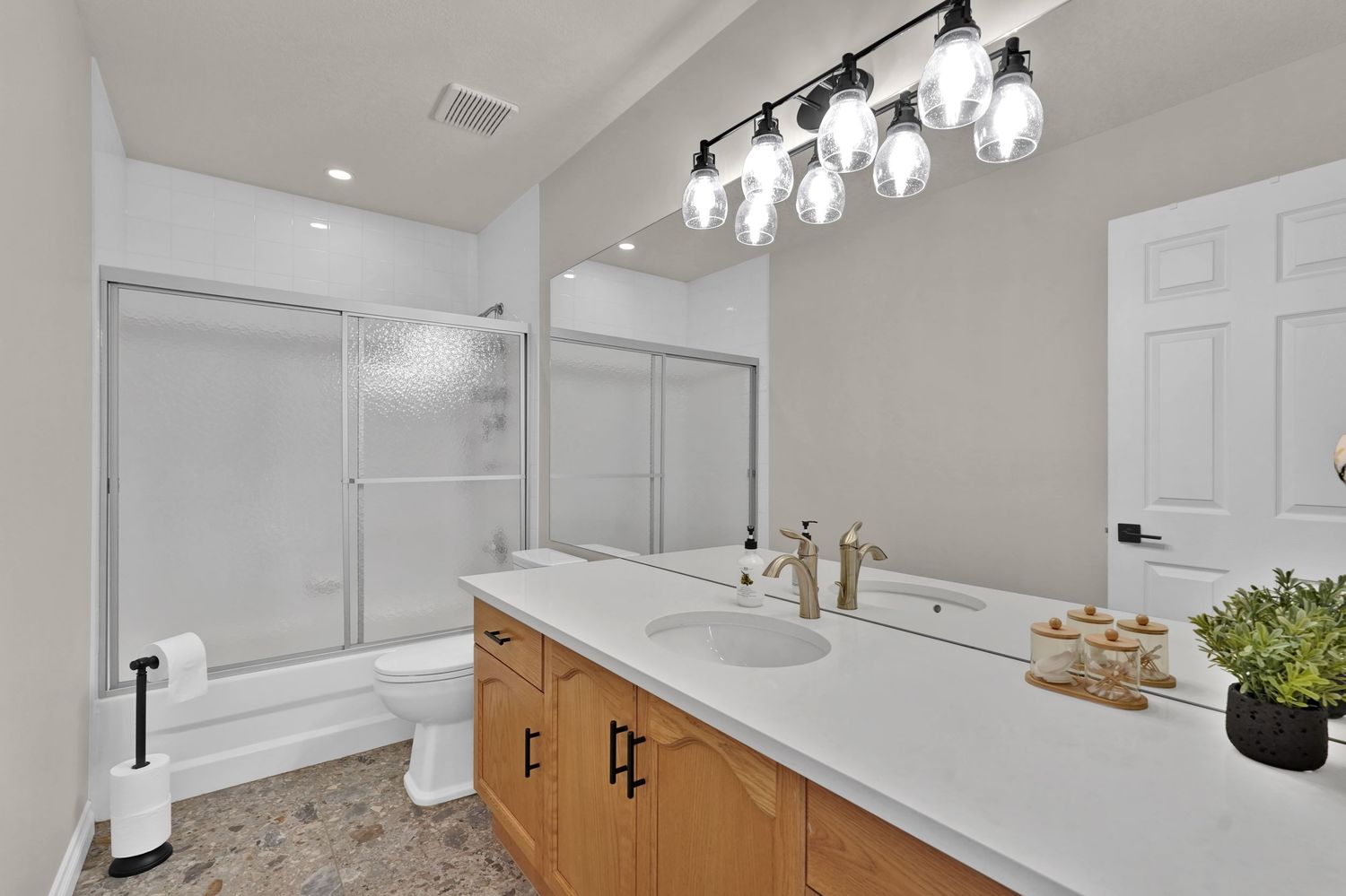 Bright bathroom with wood vanity, white countertop, glass shower, and modern globe pendant lighting.