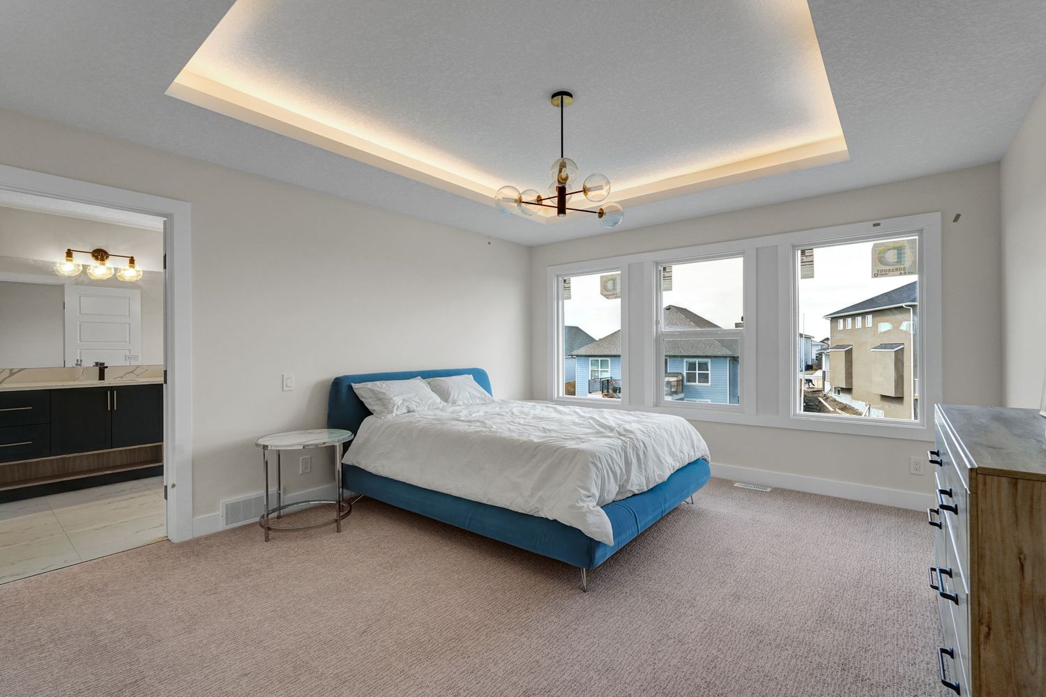 Spacious master bedroom with tray ceiling, ambient lighting, blue upholstered bed, and carpet flooring.