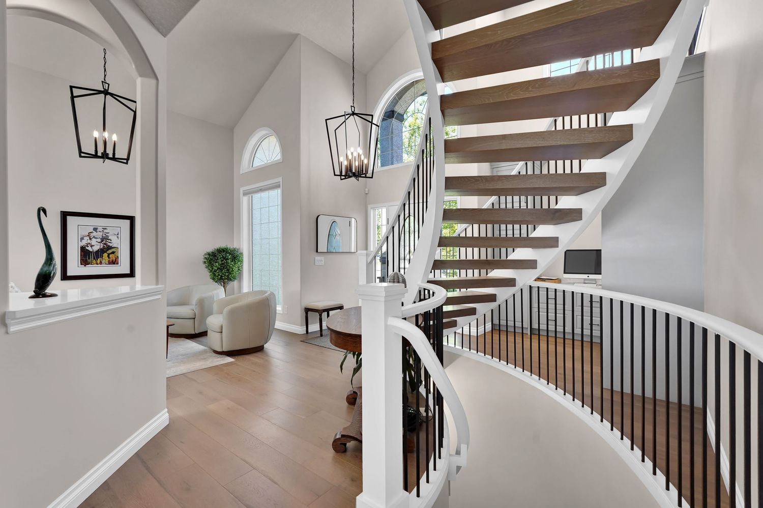 Elegant foyer with curved staircase, dark wood steps, white railings, hardwood floors, and chandelier lighting.