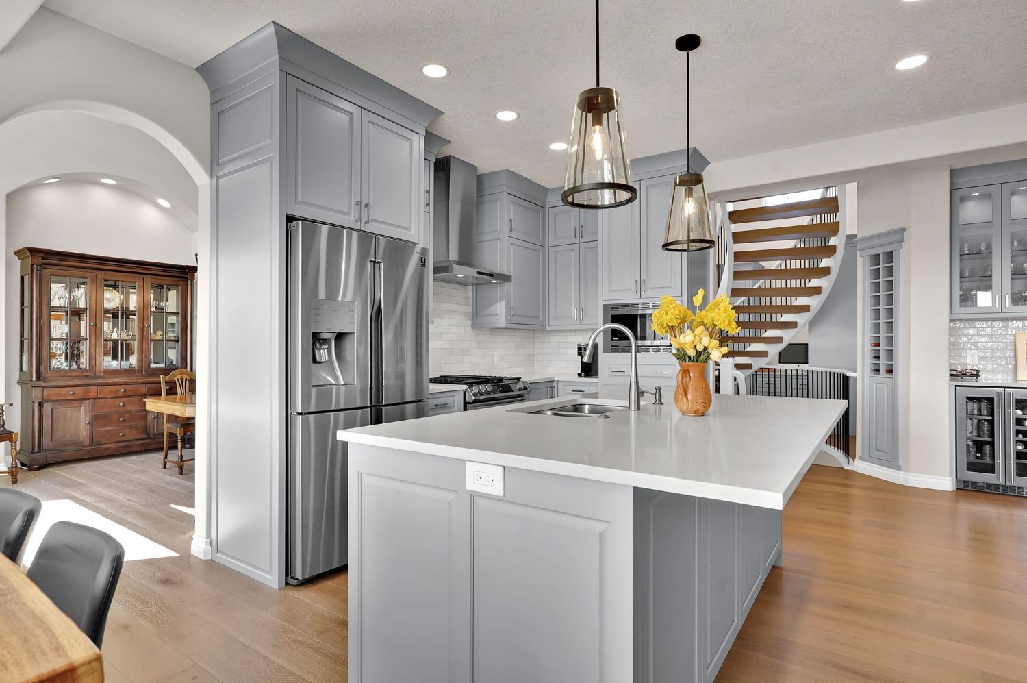 Gray kitchen with island, pendant lights, stainless appliances, white countertops, and hardwood floors in an open-concept home.
