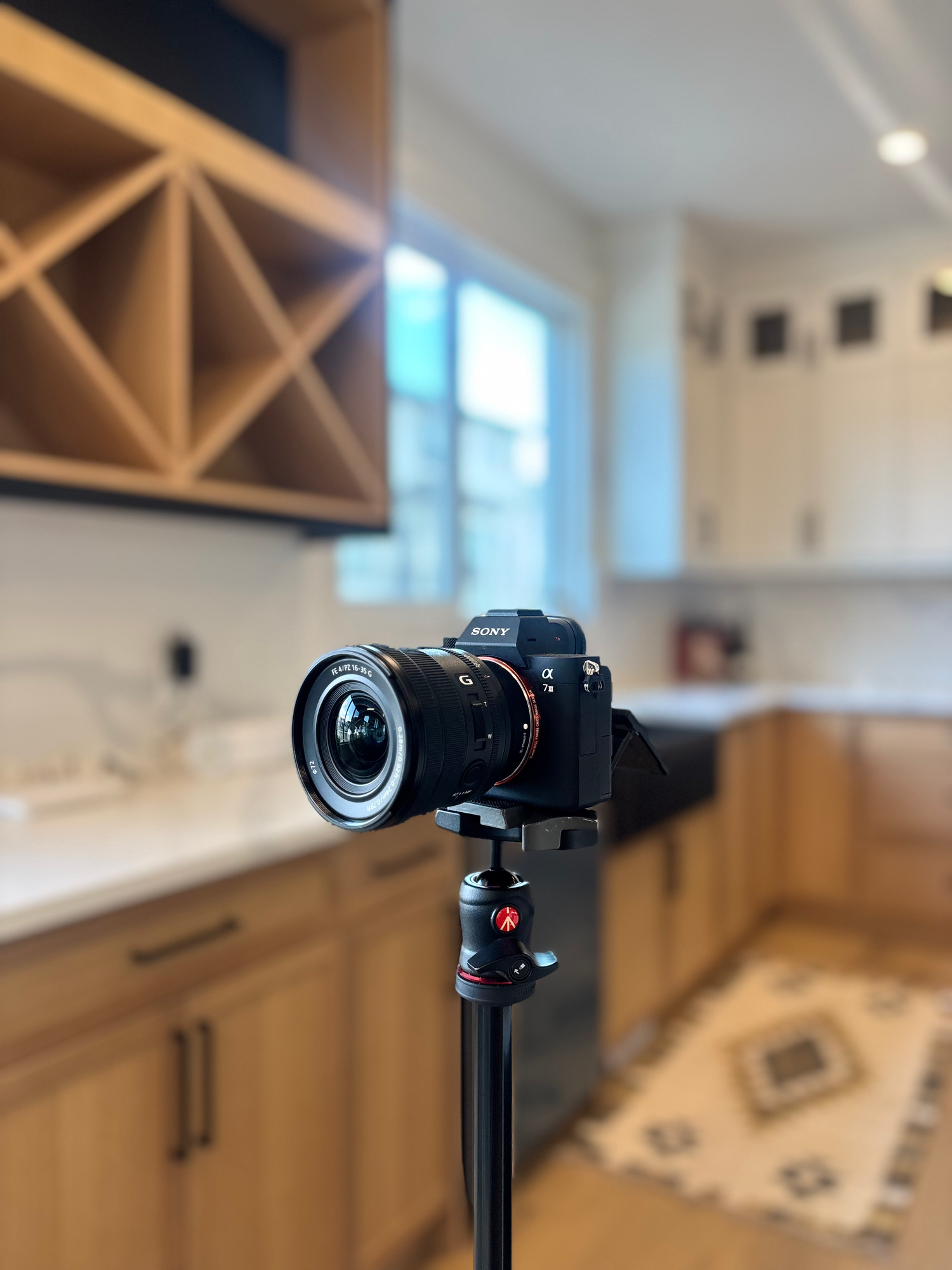Sony camera on tripod set up in modern kitchen with wood cabinets and wine rack for real estate photography.