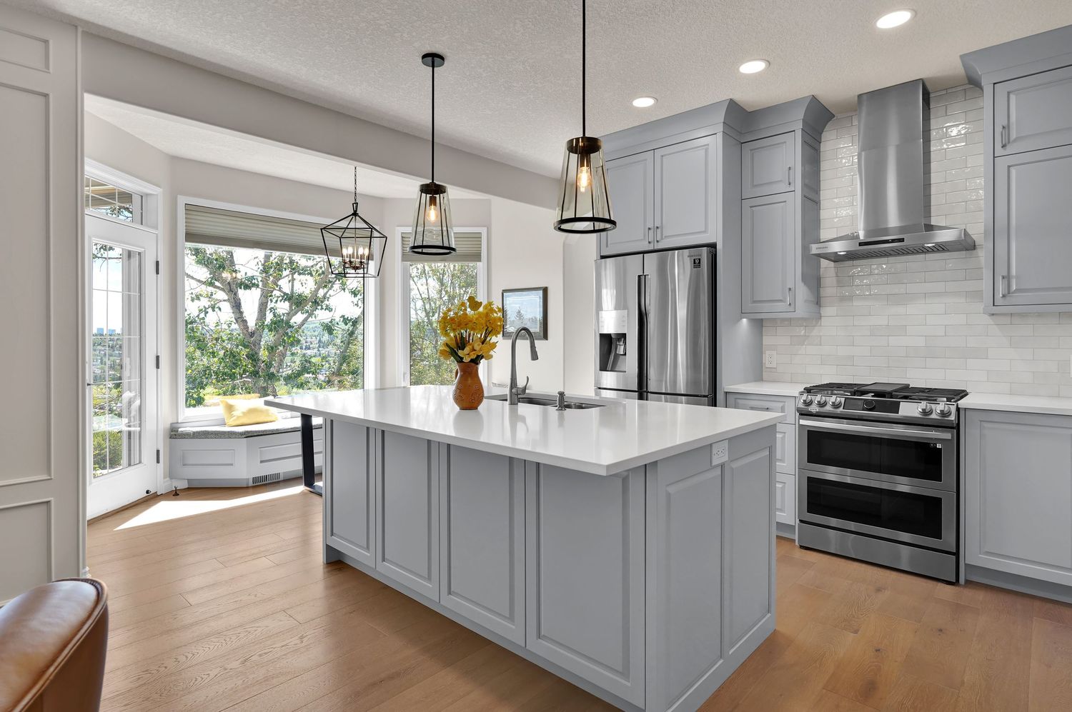 Modern kitchen with gray cabinets, white quartz island, stainless steel appliances, hardwood floors, and pendant lights.