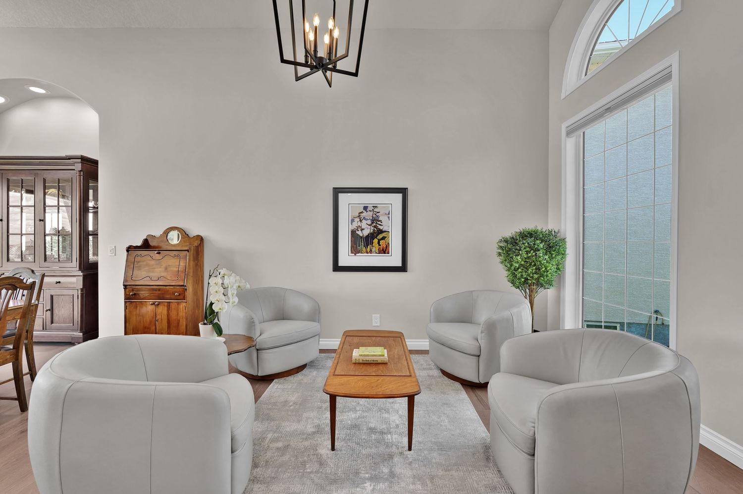 Elegant formal sitting room with high ceilings, chandelier, arched window, and light gray curved sofas.
